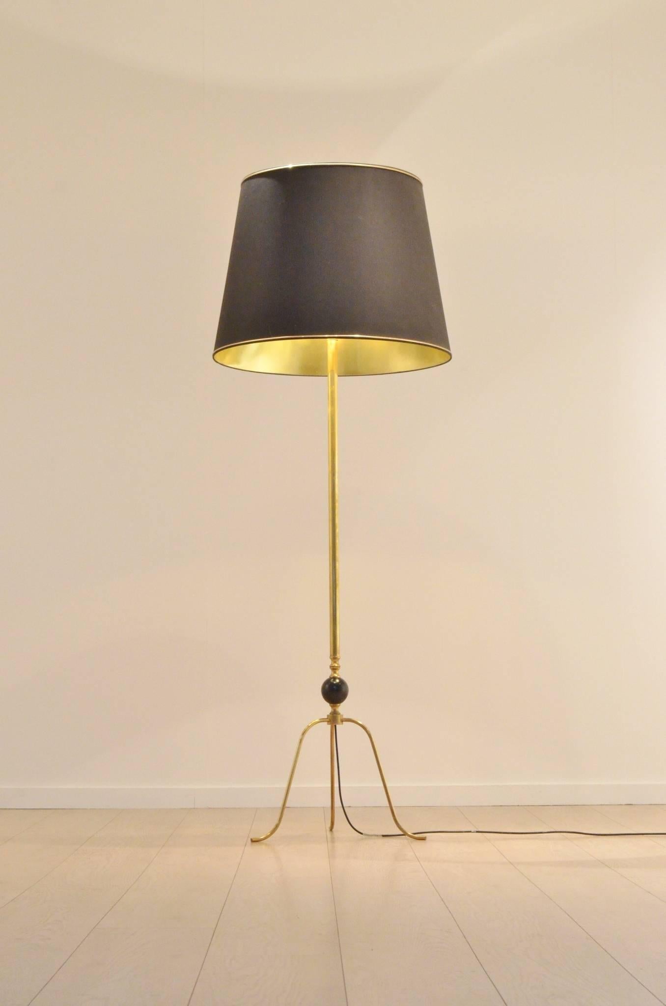 Decorative 1950s minimalistic floor lamp full brass structure and tripod feet. One black painted wood ball insertion. Black textile shade with golden inner lining.