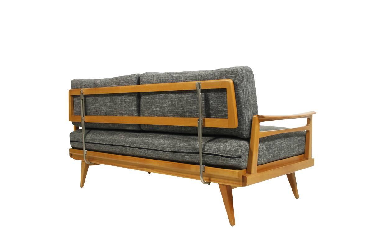 This mid century modern daybed was designed and produced by Knoll in the 1950s. It is made of beech and has been newly upholstered and covered with woven fabric. This piece has many features such as an adjustable backrest and an extendable armrest.
