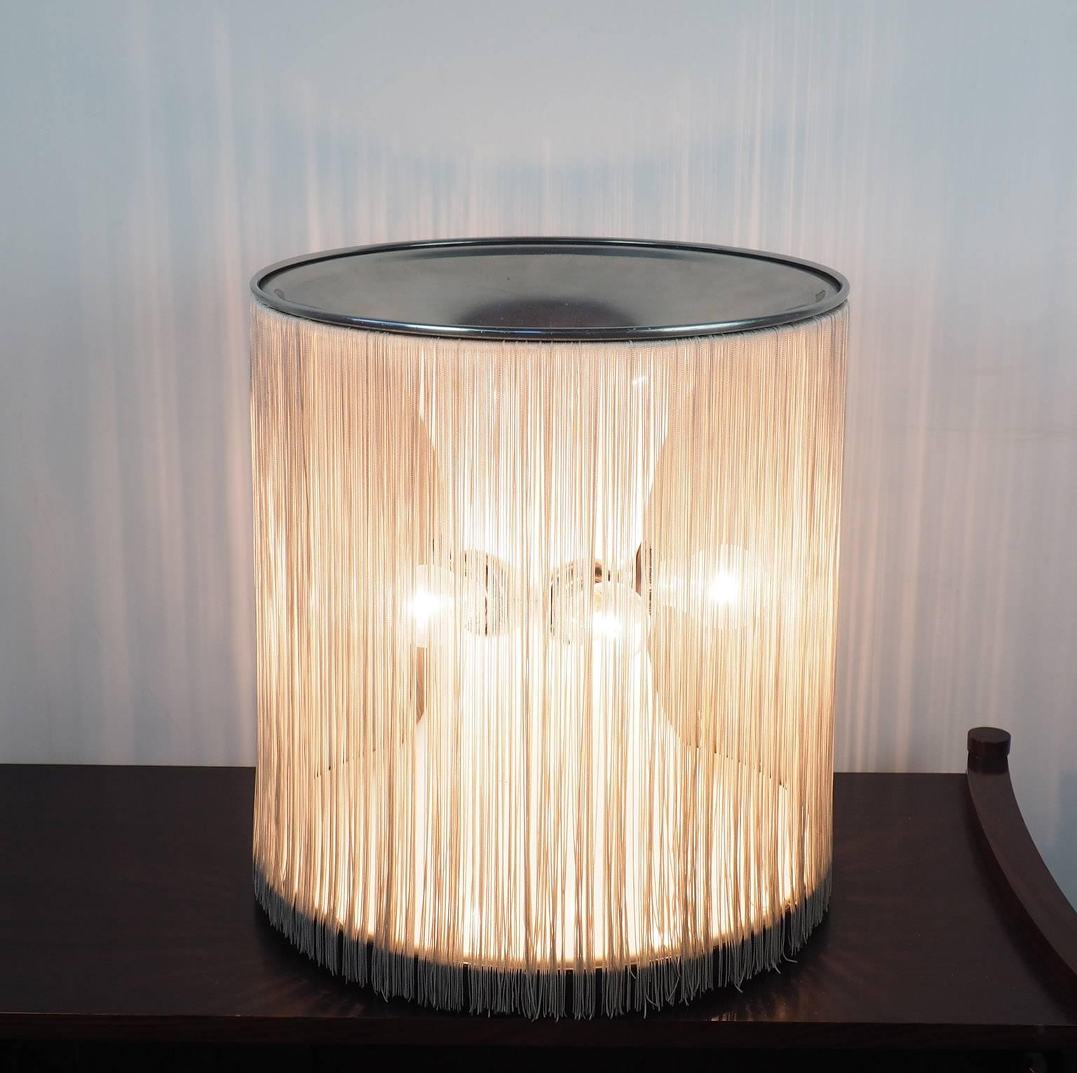 Thanks to the original silk fringe, the light becomes warm and cozy with this beautiful table lamp designed By Gianfranco Frattini in 1961 for Arteluce in Milano. Made of aluminium, (as the top that is polished aluminium as the base, that is