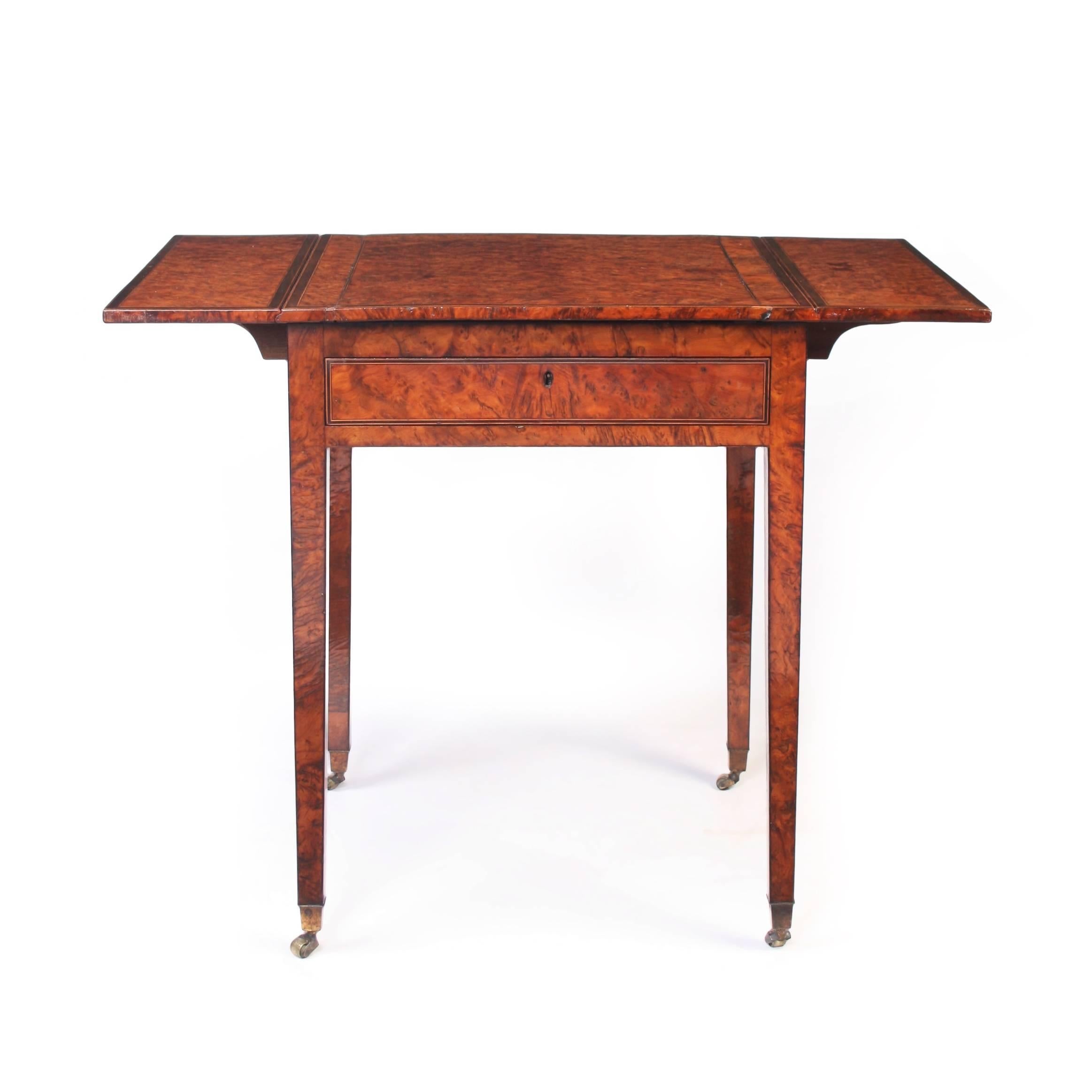 An attractive burr yew wood Pembroke table having a rectangular top cross banded in ebony and lined in boxwood, above a single drawer frieze and raised on square tapering legs and brass bucket castors.