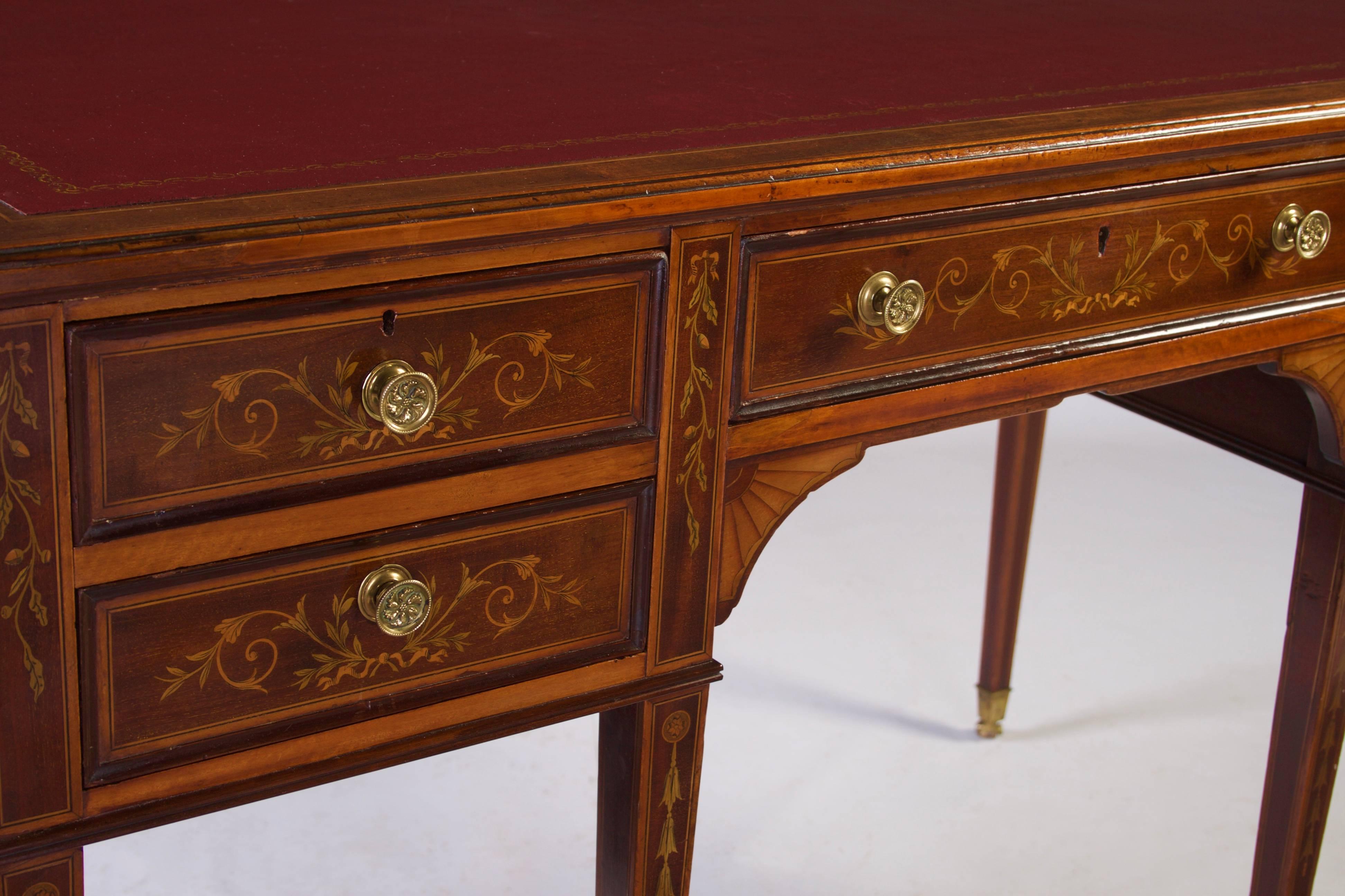 Having an inset red leather top with gilt tooling, above a central drawer stamped Edwards & Roberts, flanked by two shorter drawers each decorated with inlaid bell flowers, standing on six square tapered legs with further bell flower inlay
