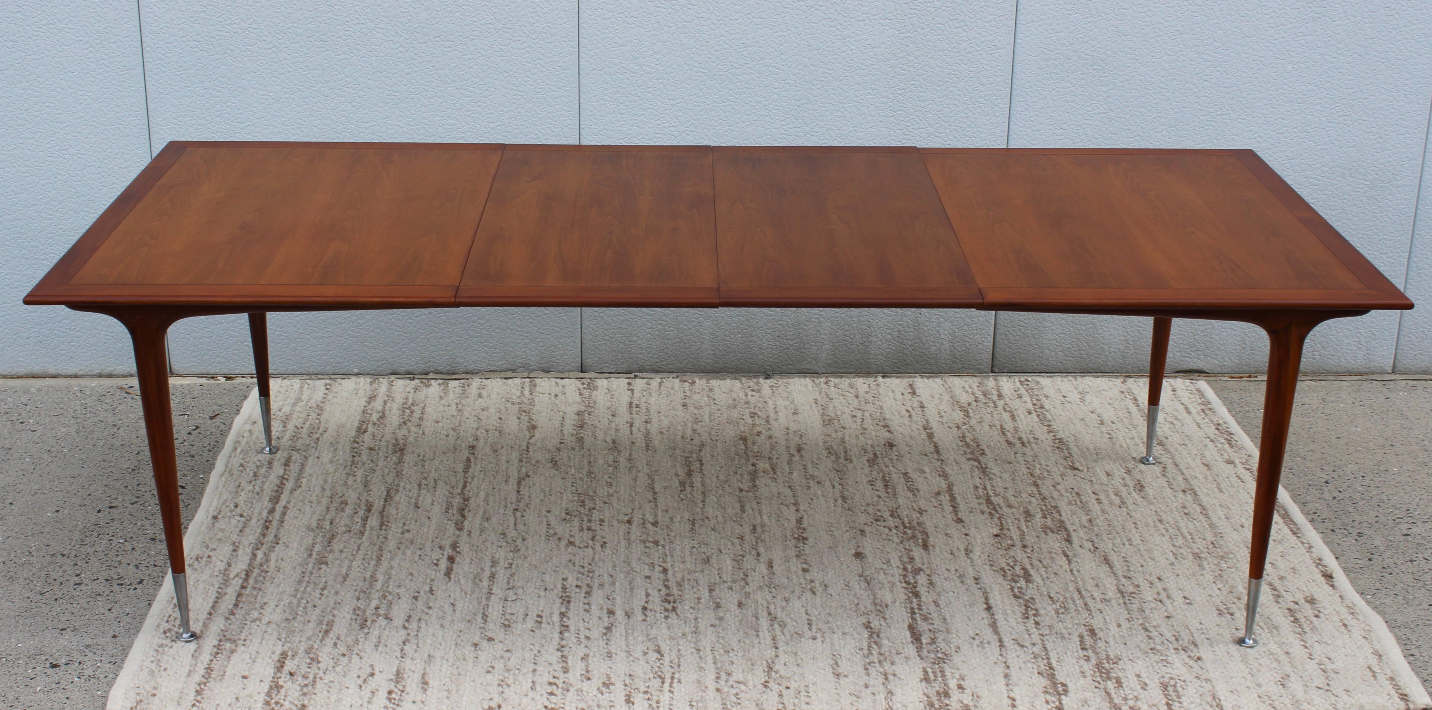 Stunning 1950s modernist walnut dining table with two leaves and aluminum sabots. 

Length without the leaves 60''.