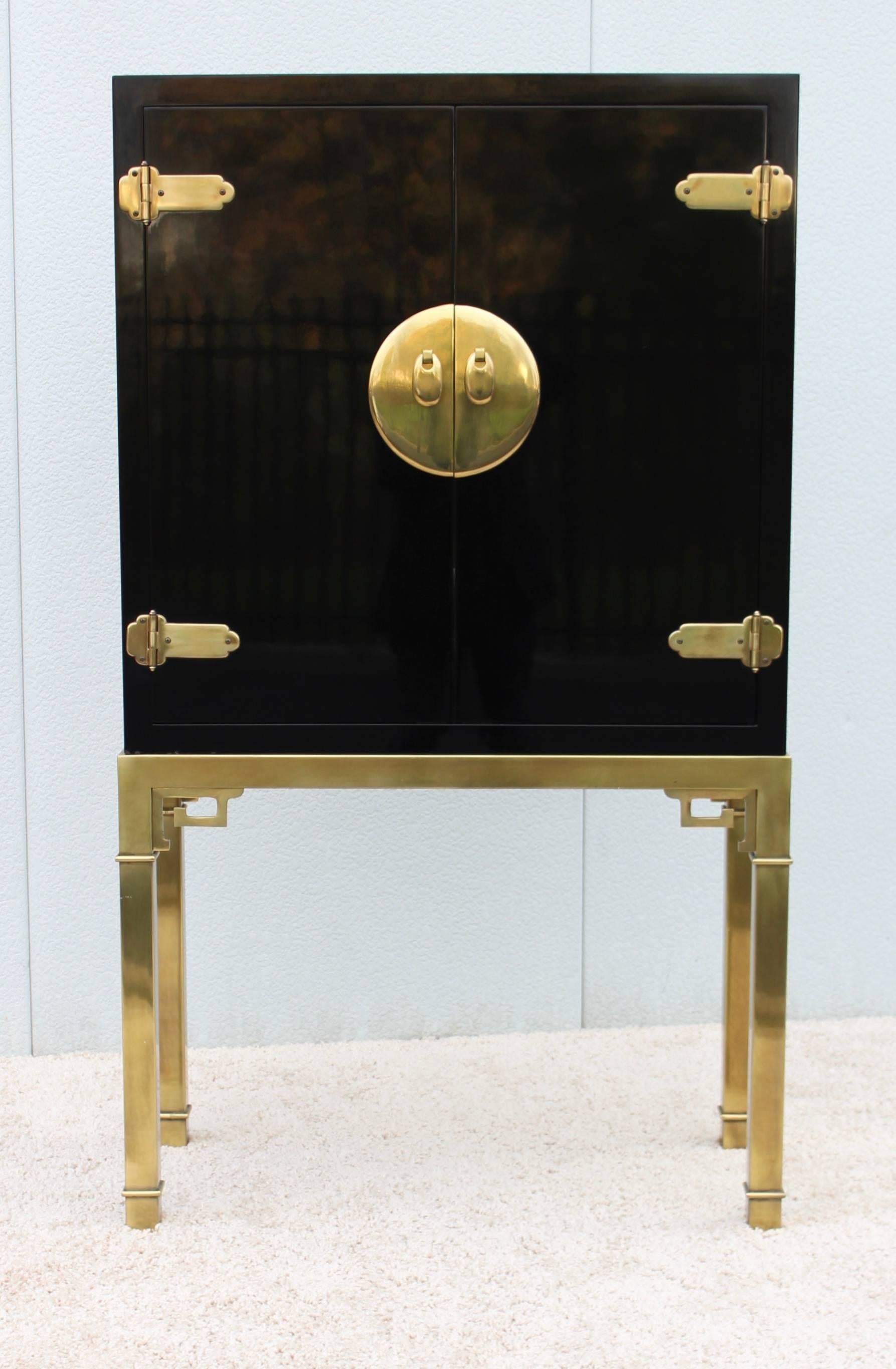 Stunning 1970s brass and black lacquered with brass Greek key base bar cabinet by Mastercraft. With doors that open to a mirror back with one adjustable glass shelf and single drawer.
