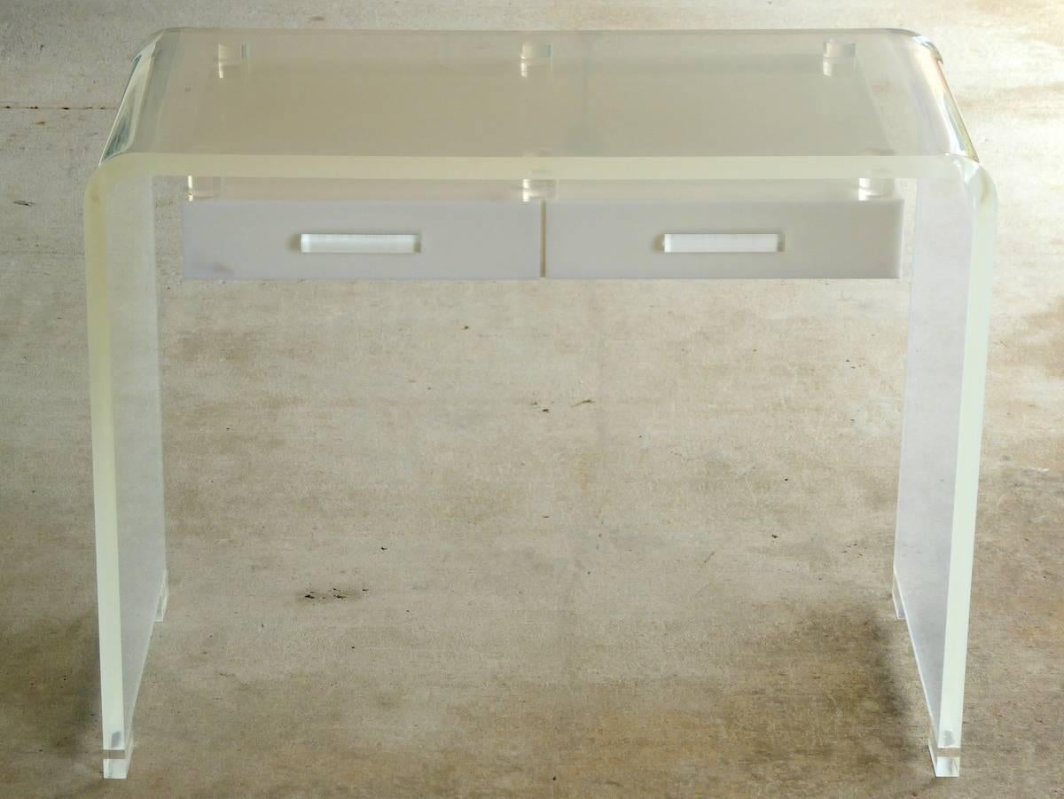 A delightful two-drawer waterfall desk or vanity in a mixture of clear, semi-opaque, and white Lucite. The main arch of the desk is semi-opaque. The drawer assembly is white. And the drawer pulls and feet are clear. Stunning.

We have an extensive