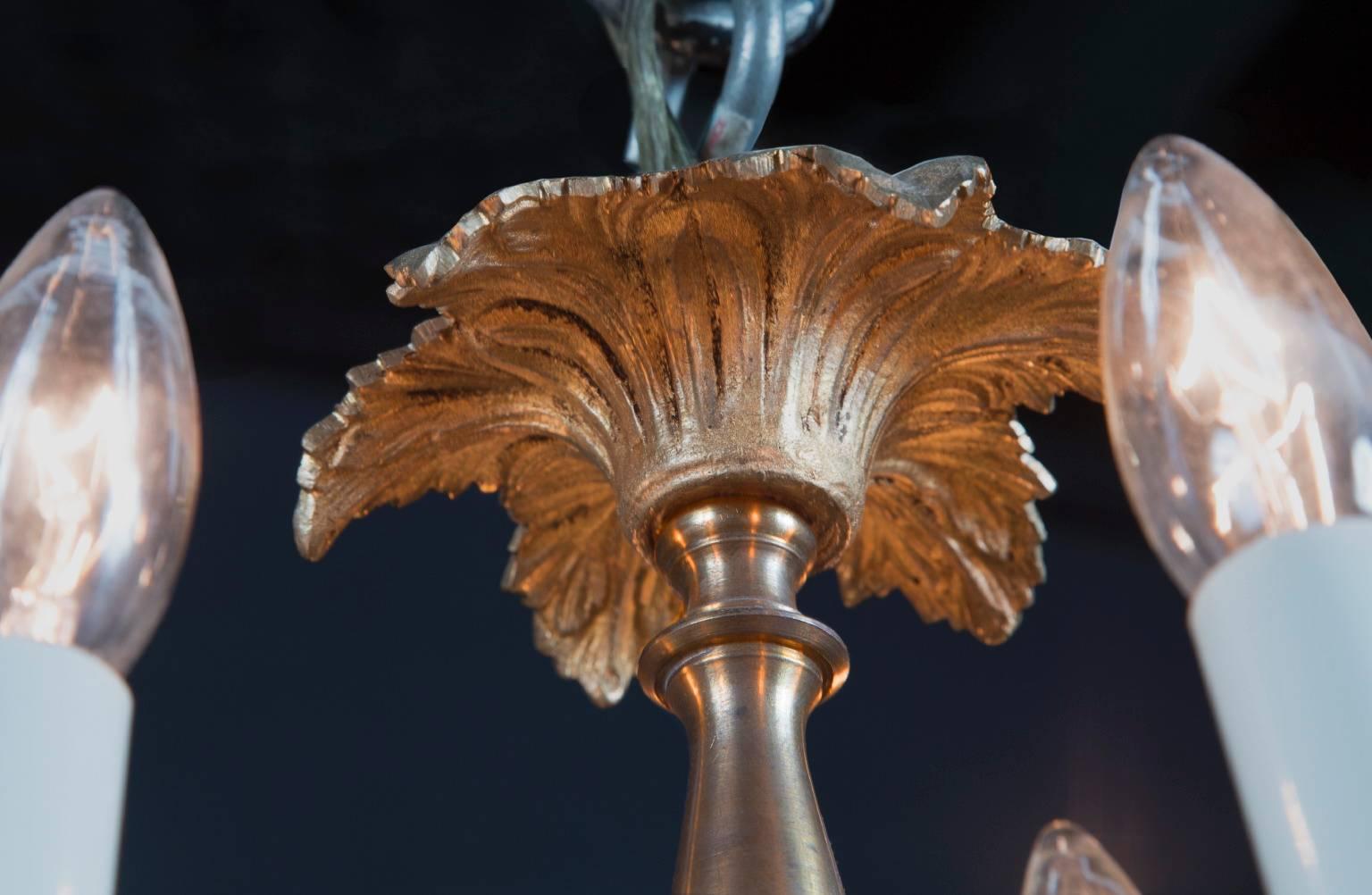 This Louis XVI bronze chandelier features bronze leaf  bobeches, a style mirrored in the crown of palm fronds at top. The 19th century French antique piece sports bronze scroll arms adorned with leaves, as well as a bronze center. The chandelier is