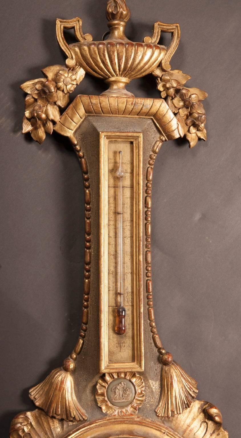 Made of hand-carved wood in 18th century France, this barometer is elegantly covered in a variety of carved designs, all coated in gold leaf. A handled Grecian vase sits atop the stem of the barometer, with a pair of carved tassels hanging down