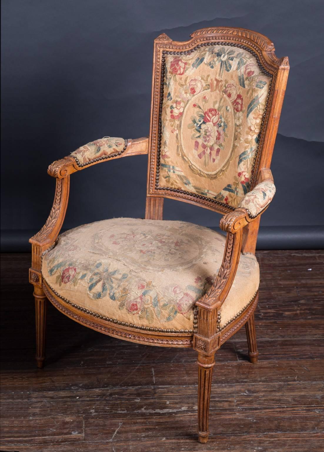 This pair of French Louis XVI open arm chairs (fauteuils) features beautifully carved walnut and dates back to the 19th century. The hand carving is truly fantastic, with delicate details found in the block marguerites, acanthus leaves and pattern