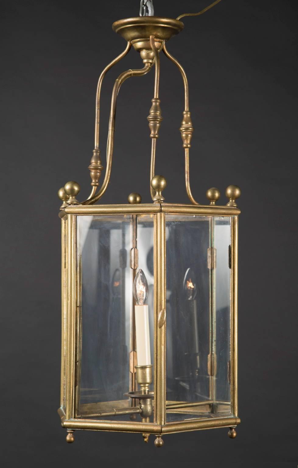 Cette lanterne hexagonale Louis XVI est en laiton et comporte une porte et une lumière intérieure. Cette pièce antique française date du XIXe siècle et est décorée d'un bouton à chaque coin du plateau. Des boutons plus petits reposent à chaque coin