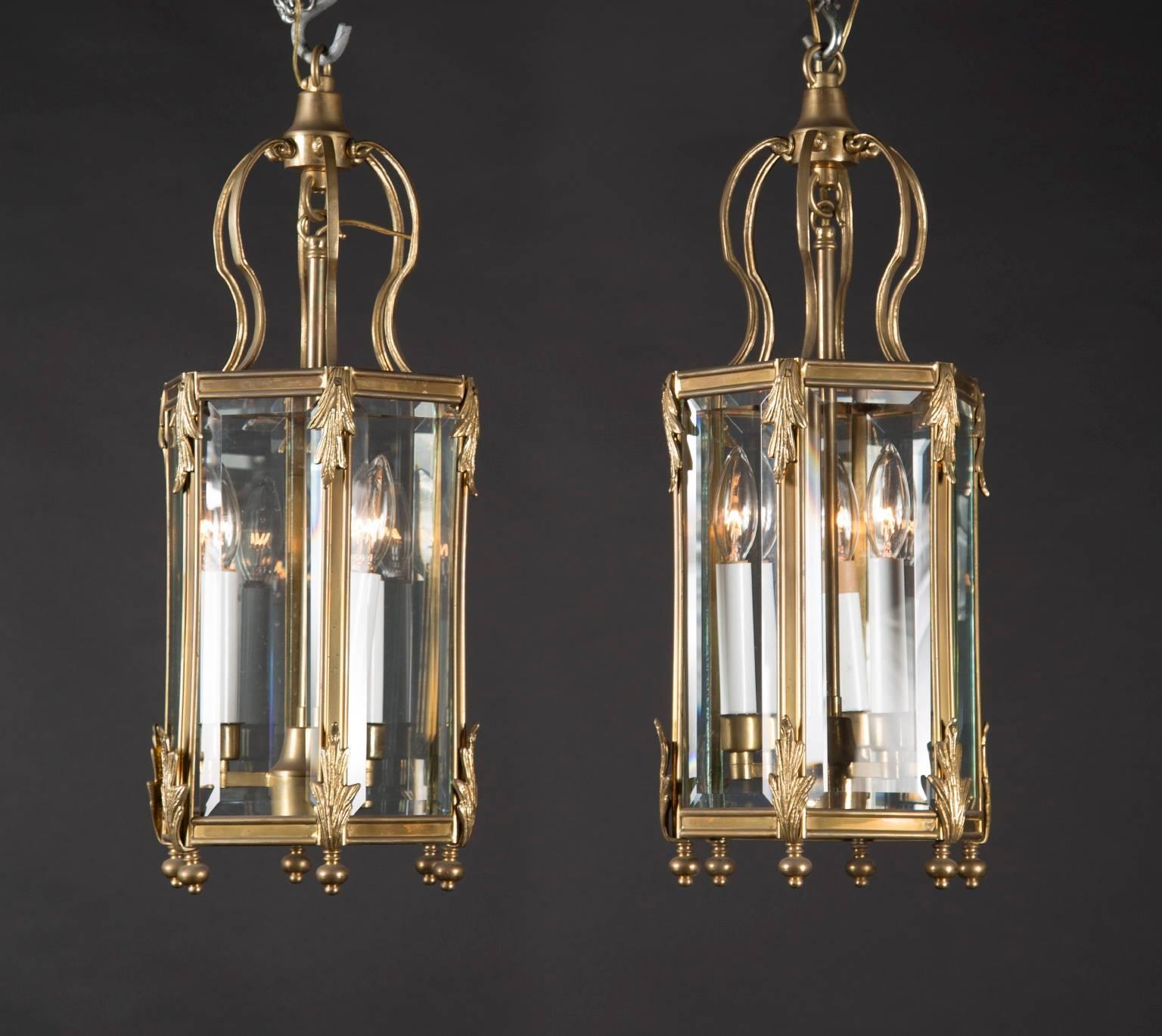 This pair of hanging lanterns is made from bronze with six panes of beveled glass on each fixture. A rounded bronze finial sits at the base of where each pane intersects. Curving arms hold the body of the lantern to a bronze crown, with a central
