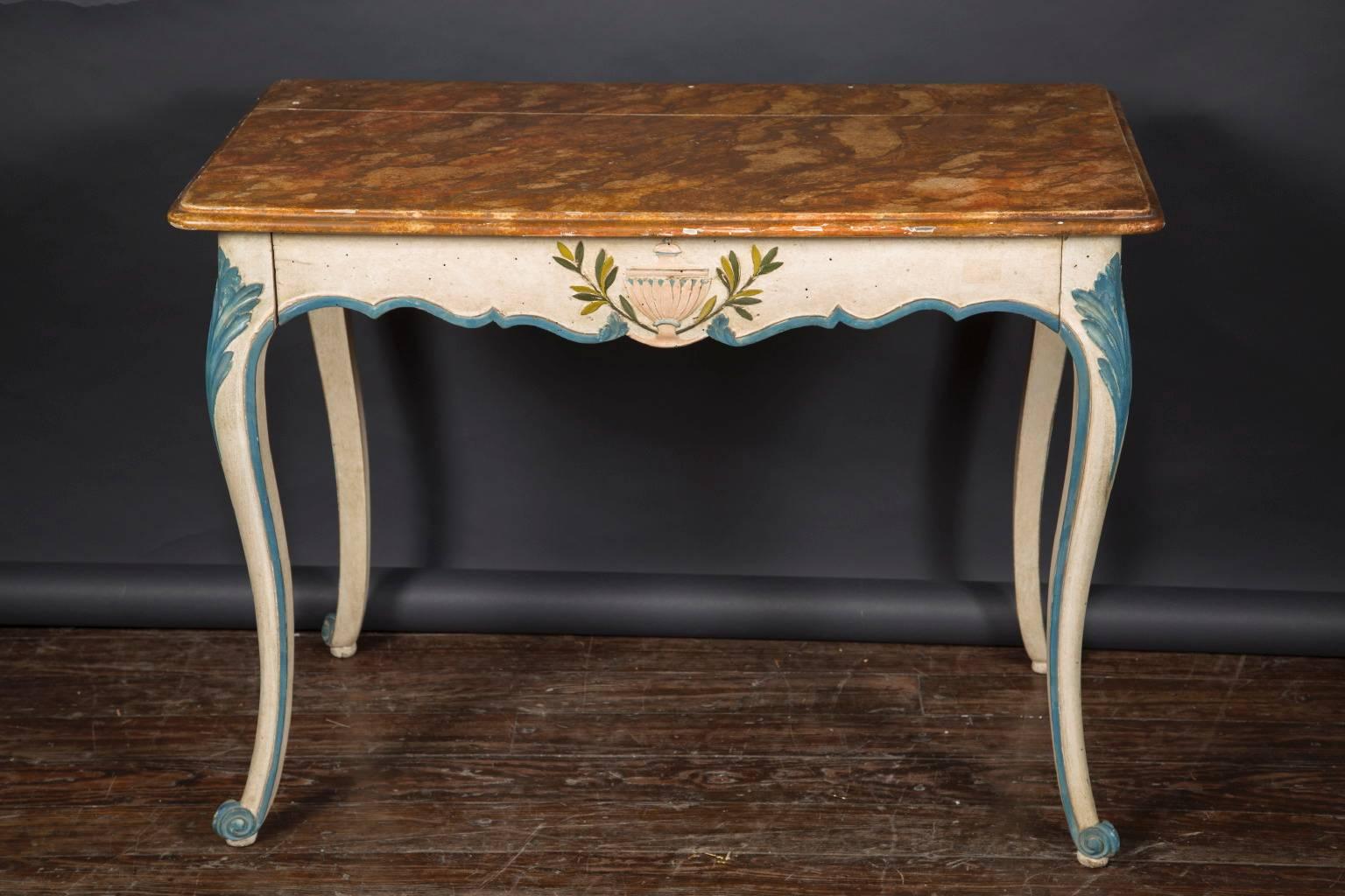 This Italian Louis XV console table is beautifully carved and painted in the classic revival manner. The piece dates back to the early 20th century and rests on four cabriole legs, scroll feet, and hosts a faux marbre top.  The table has an urn with