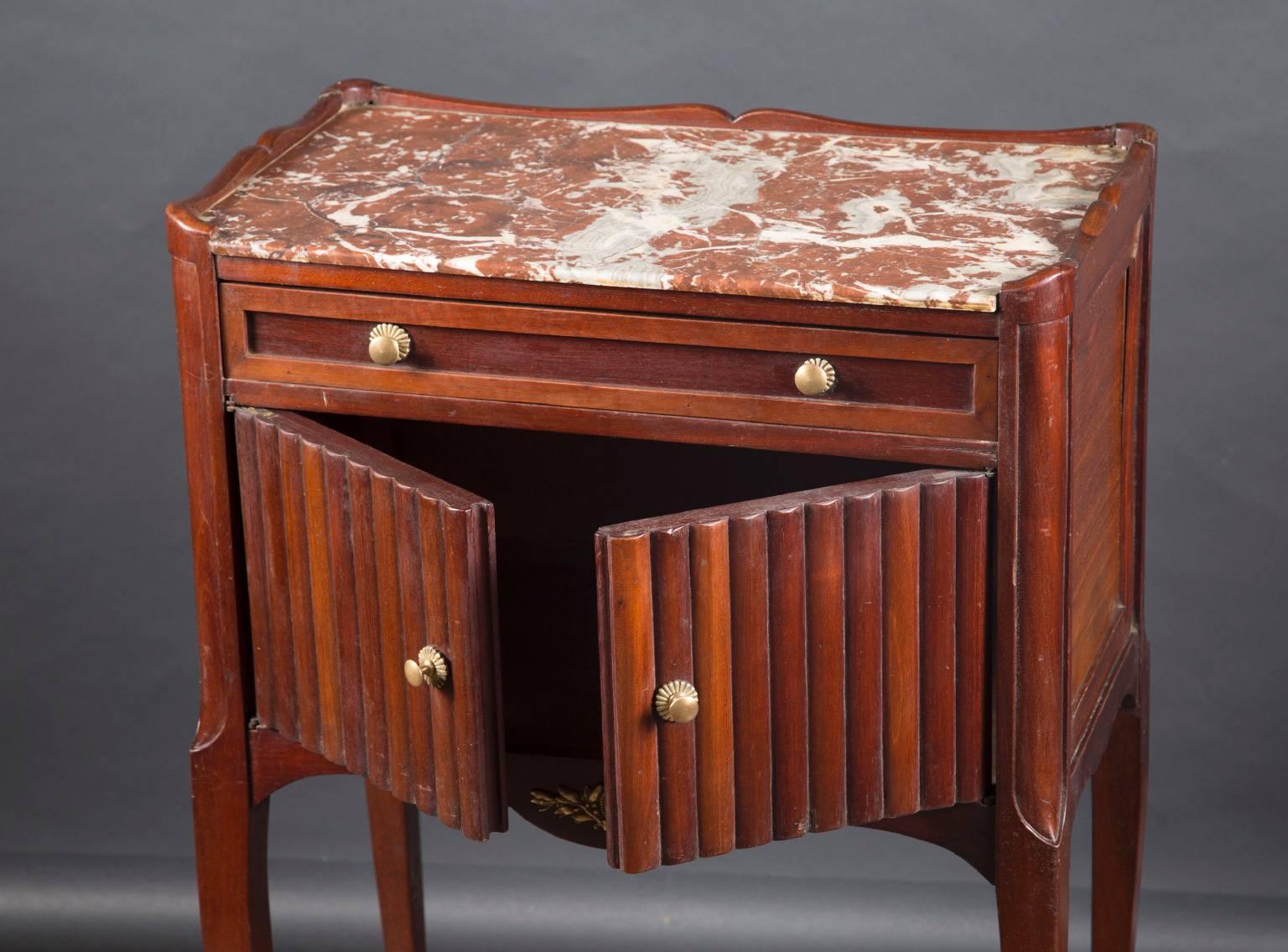 This bedside table was handcrafted in 19th century France from mahogany wood. It has a pullout drawer on top of two wood slat doors which open for storage space below the drawer. A slab of marble rests on top the table creating a beautiful useable