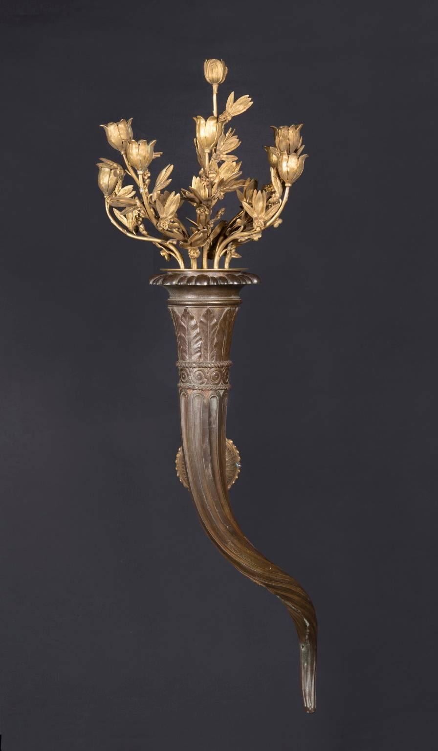 This pair of fantastic French bronze sconces feature most notably at top a bouquet of eight bronze d’ore candle holders. Dating back to the 19th century, the pair offers a beautiful spiraling “Horn of Plenty” base, with an egg and dart motif around