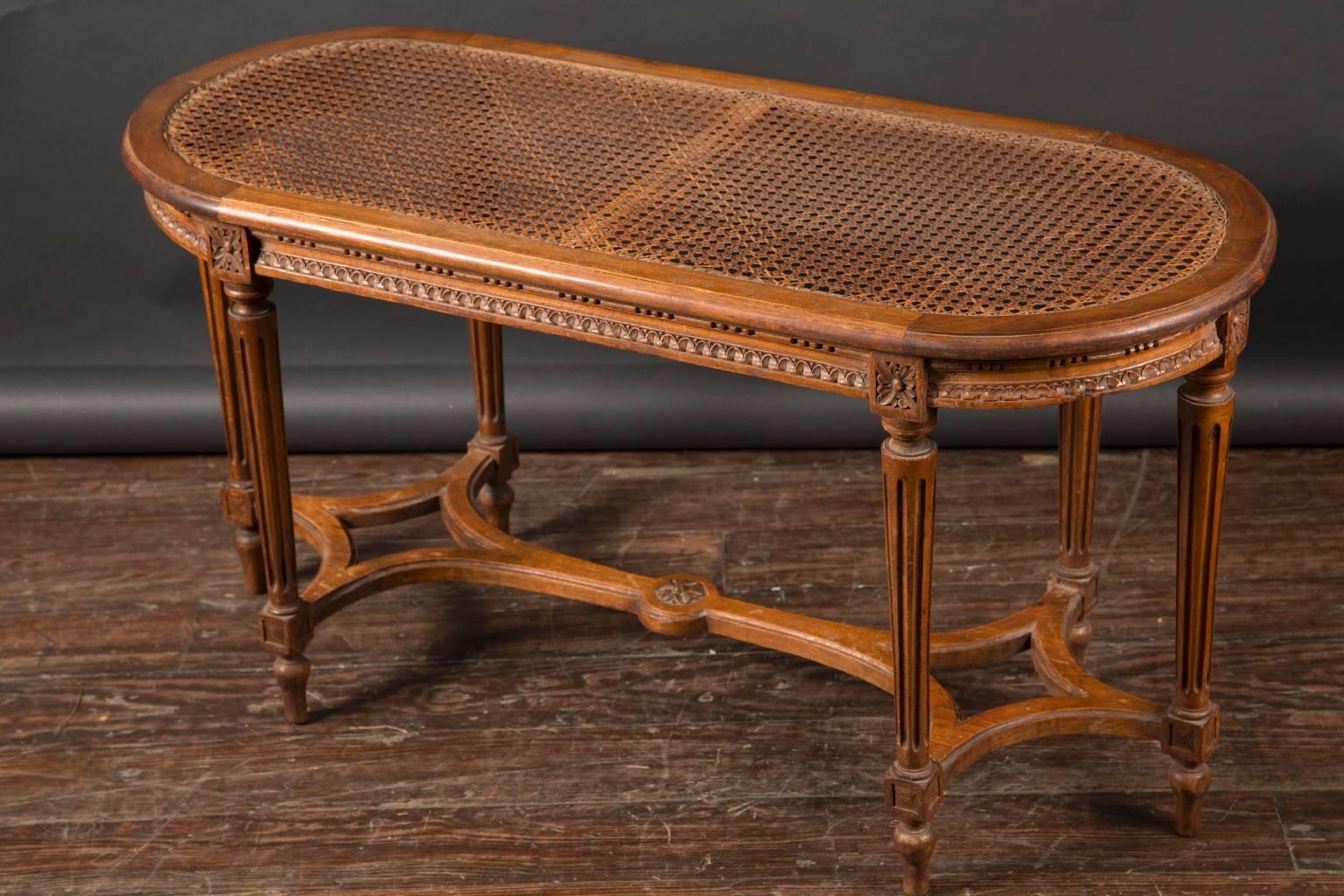 This beautiful Louis XVI bench is made of walnut and features a caned seat atop 6 fluted legs. The French antique piece dates back to the 19th century and offers small block marguerites both at the top and bottom of the fluted, tapered legs.