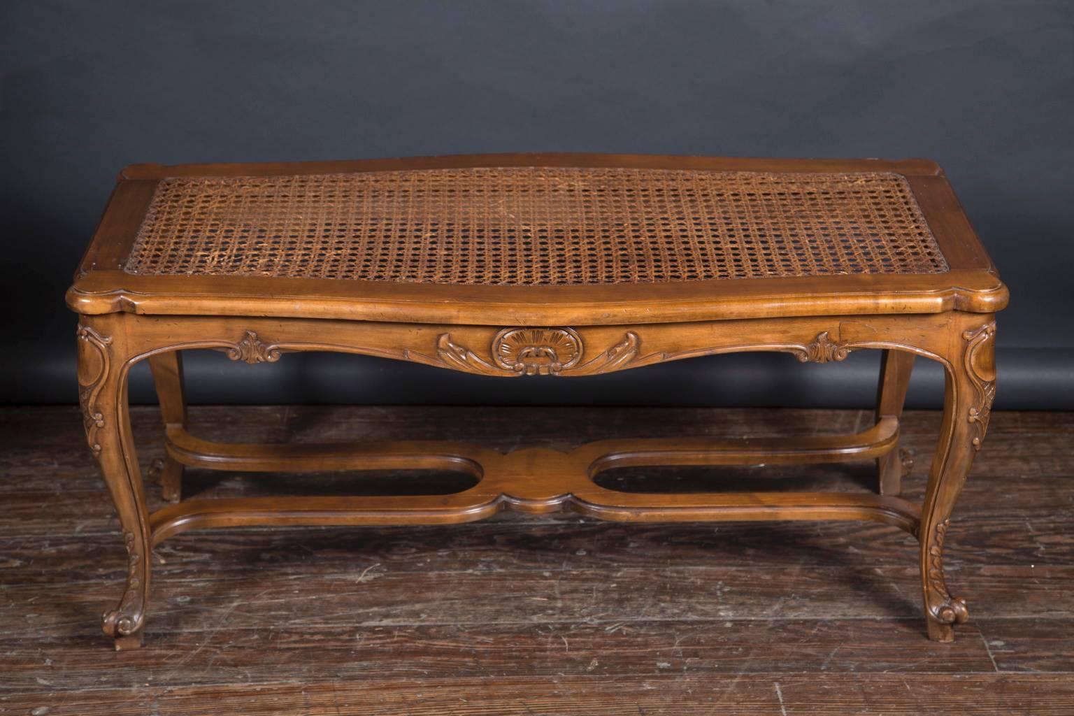 Made of a walnut frame with a caned seating area, this walnut bench has cabriole legs with scroll feet separated by a stretcher. Beautiful designs are carved into the wood of the bench along the sides and legs. The French piece dates back to the mid