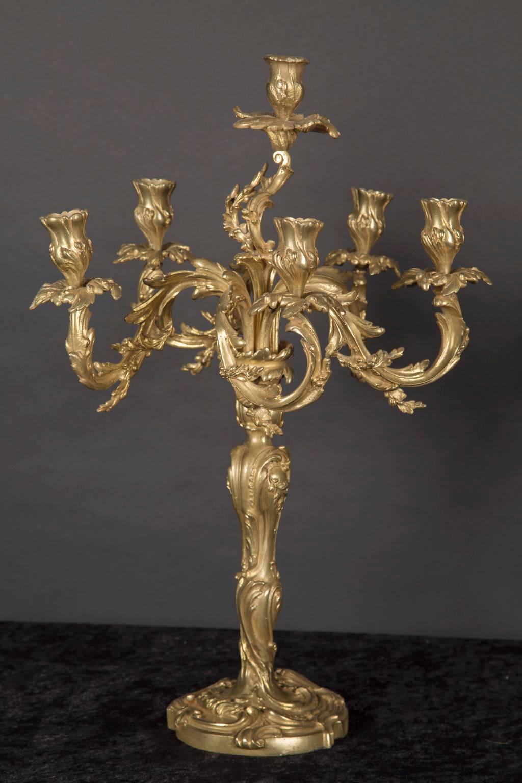 This grand pair of bronze d’oré candelabra features floriate candle cups, leaf bobeches, and arms in the classic Rococo style. The French antique pair dates back to the 19th century and sports a center stem & foot also decorated in a floriate manner