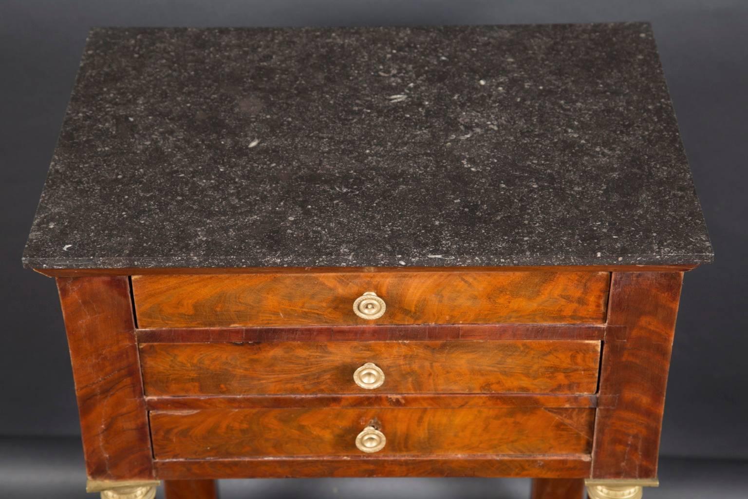 This classic Empire table is made of walnut with a dark grey marble top. The French antique piece dates back to the 19th century and sports cylindrical column legs with bronze feet at the bottom and bronze capitals at its top. Three drawers rest