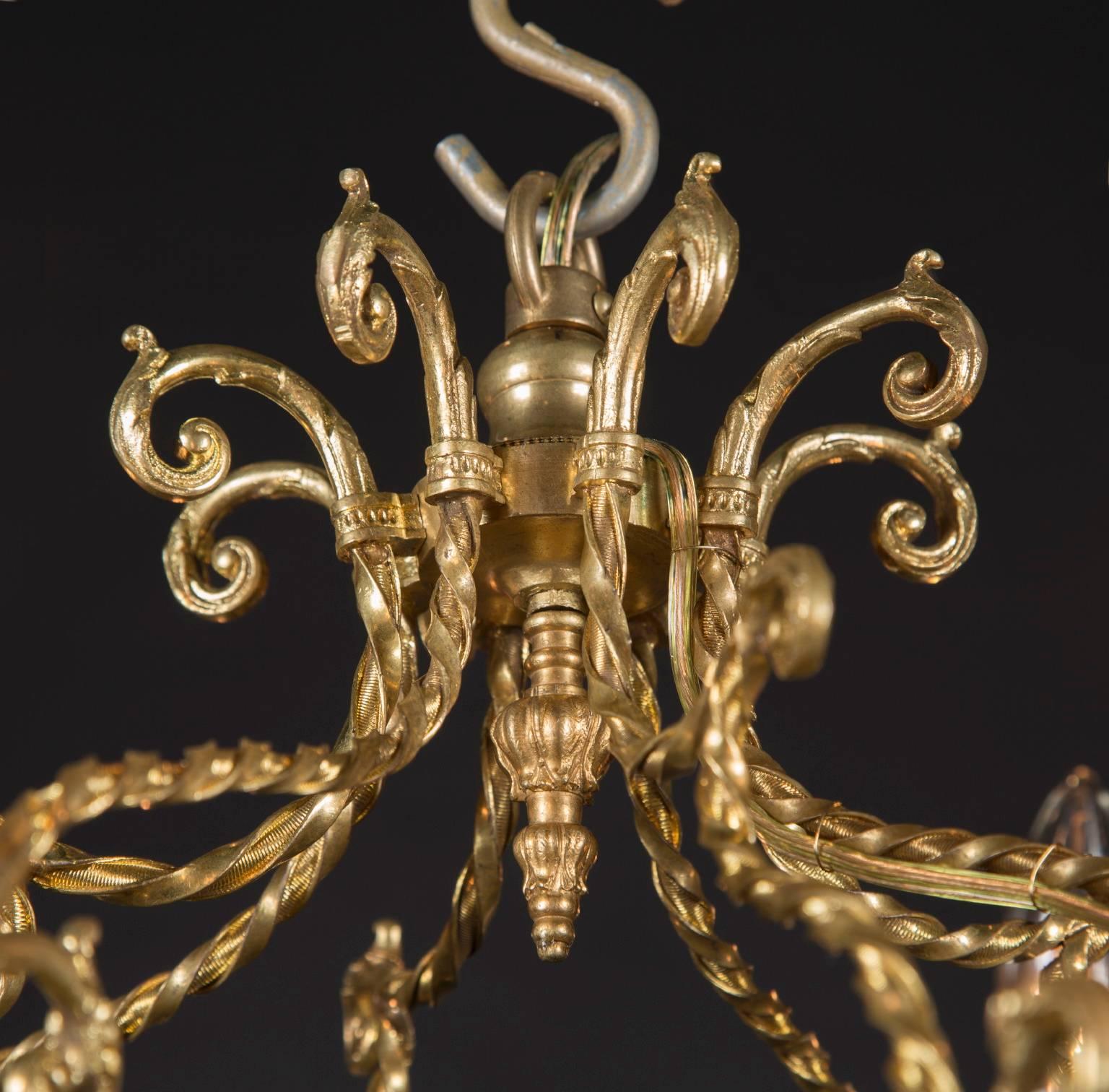 Ce lustre français ancien de style Louis XVI est composé de bronze d'or et d'un motif unique de volutes. La pièce date du milieu du XIXe siècle et a été fabriquée à la main avant l'ère de l'industrialisation. La pièce comporte des coupes de bougies