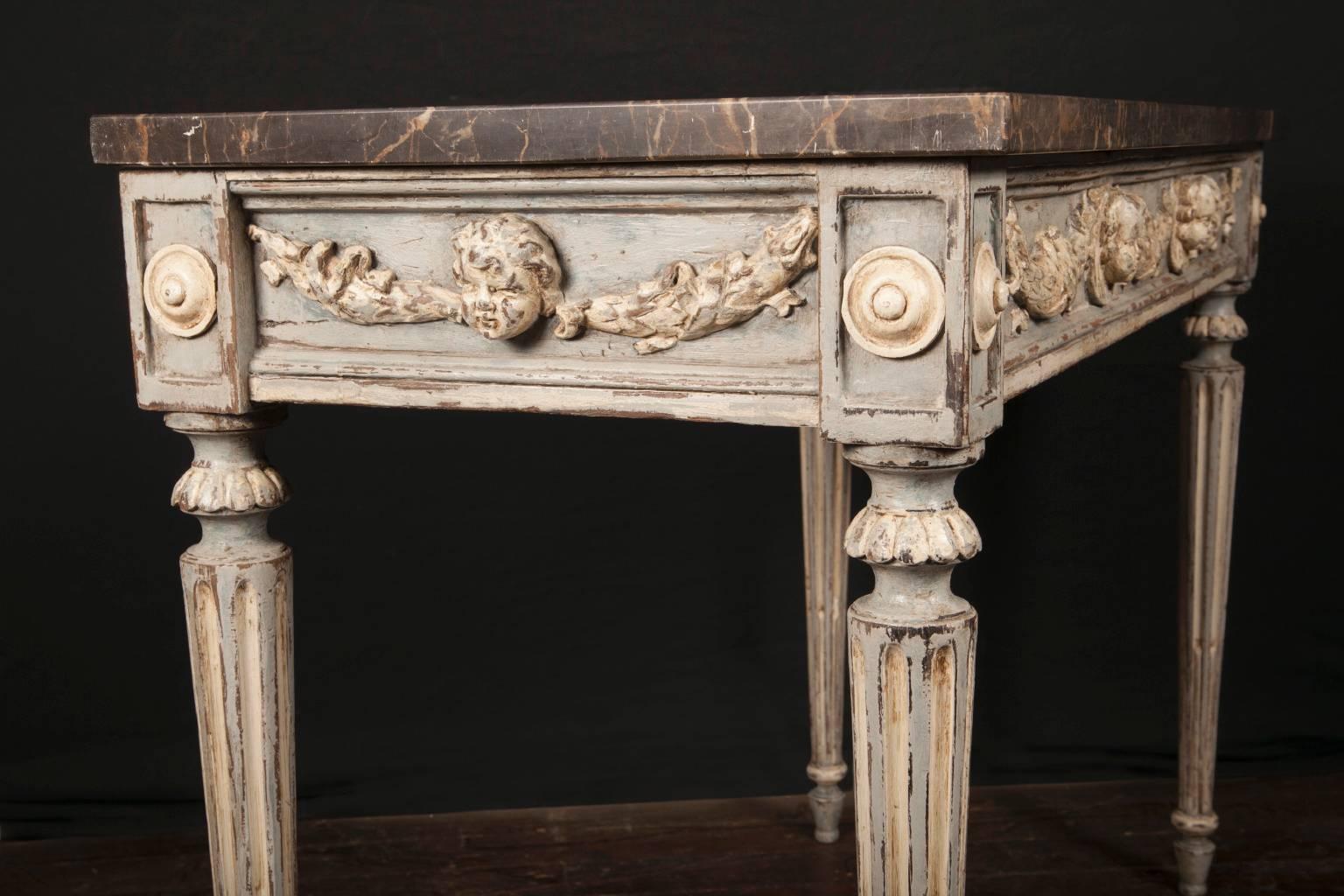 Handmade in the 18th century, this pair of antiques consoles is topped with a beautiful piece of gray marble with brown undertones and veins of white running through them. The consoles are made to be placed against a wall, with carved decorations