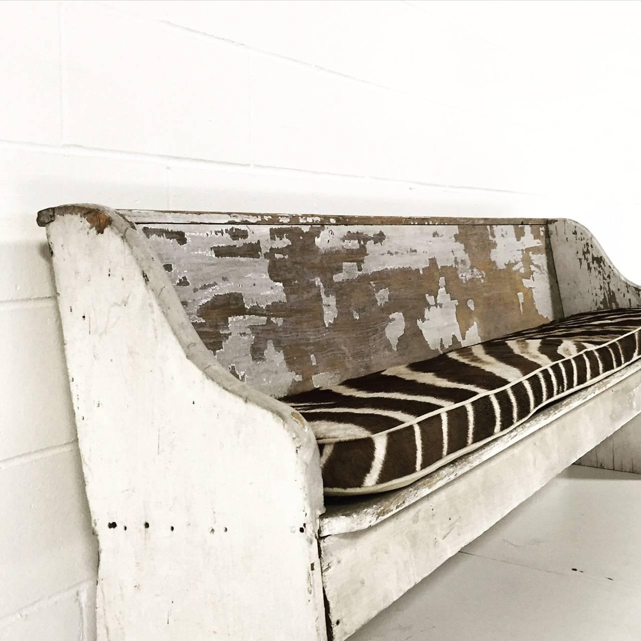 Estimated to be over 80 years old, this church pew has a time-worn patina only achieved from decades of use. The zebra cushion creates a comfortable seat, perfect for a large dining table!
