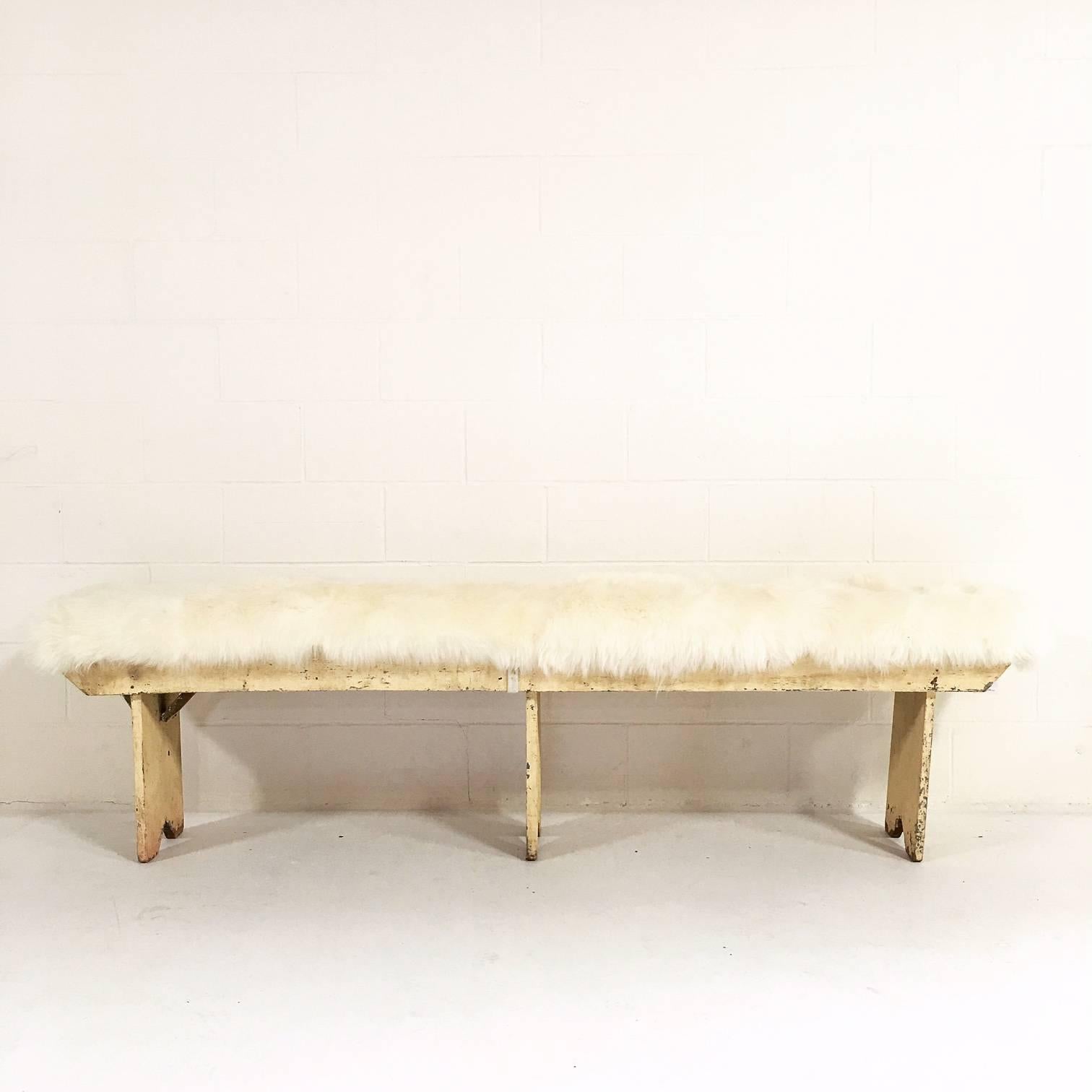 An absolutely charming farmhouse bench with a beautiful creamy paint patina. Forsyth designers selected cozy sheepskin for the cushion. The sheepskin cushion is attached to the bench with ivory leather straps. It's the perfect bench for the end of a