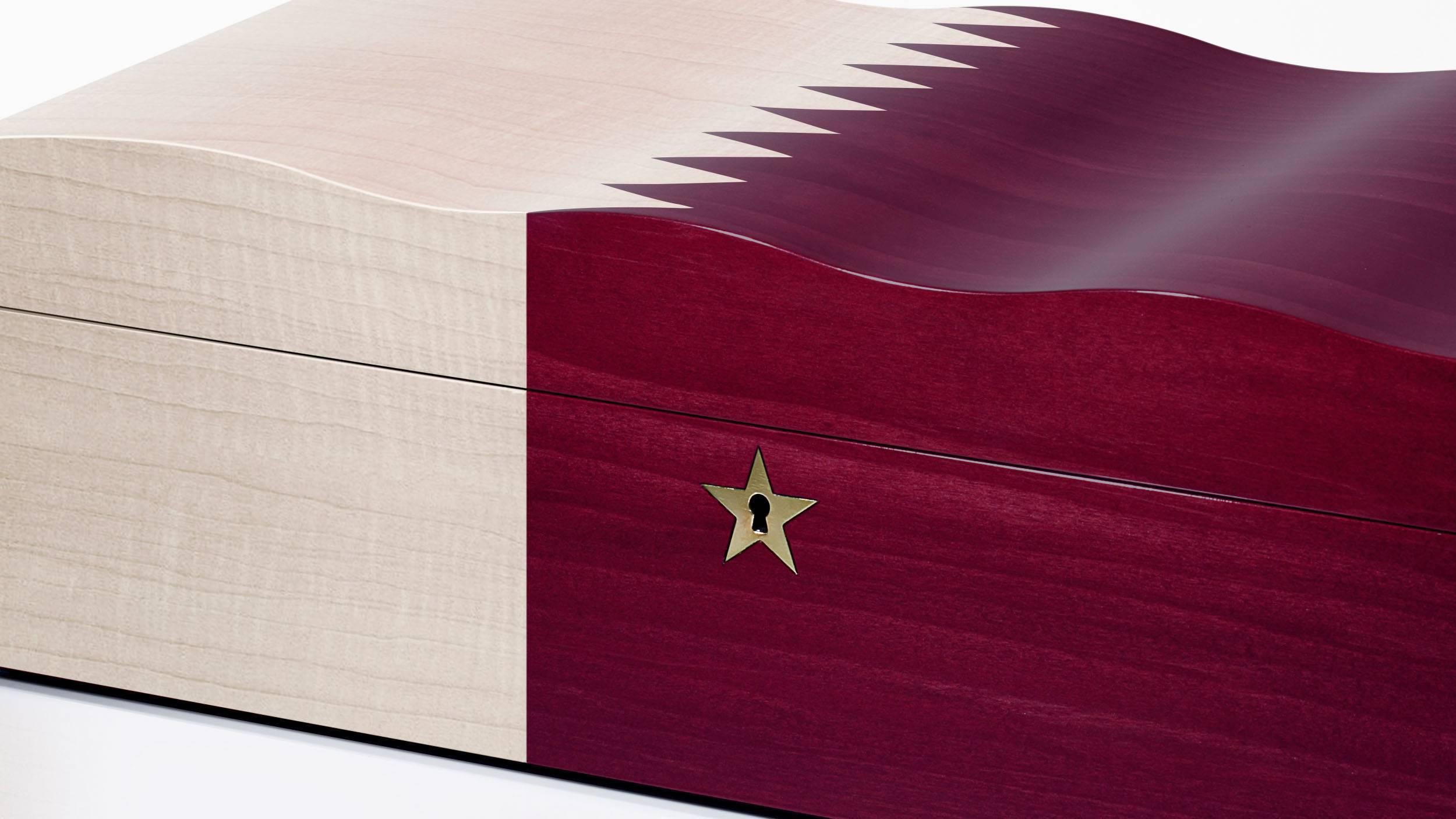 A humidor featuring the Qatari flag, constructed in dyed walnut with a burnished finish. 

The boxes are distinguished by an undulating ripple effect on the surface to evoke a flag fluttering in the wind. The humidor is lined with Spanish cedar