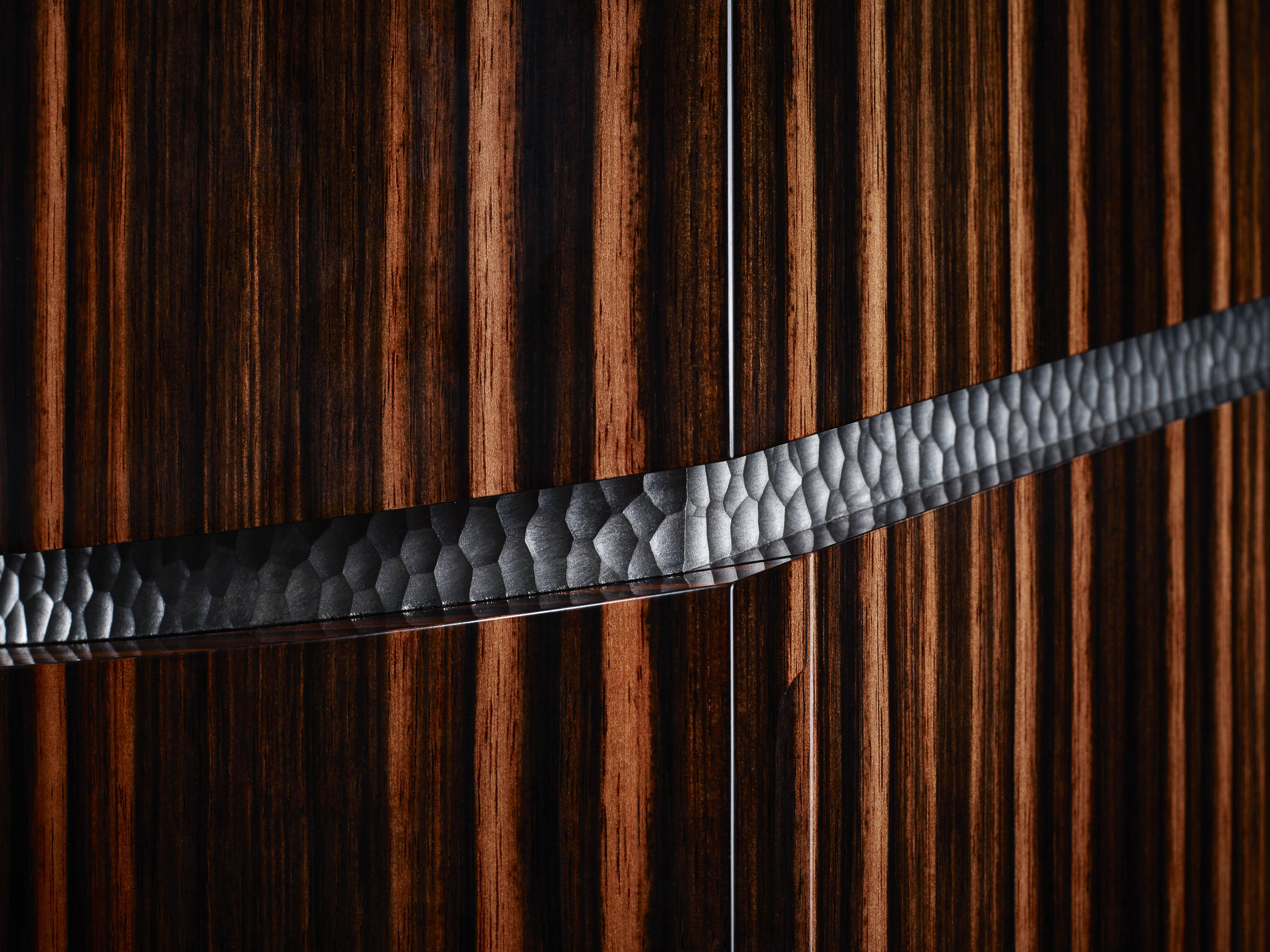 Le Penman's Box a été magnifiquement fabriqué à la main dans une combinaison de deux bois, le frêne ondulé et le noyer, et est souligné par des détails en métal nickelé. L'extérieur de la boîte est plaqué en frêne olive ondulé sur la partie
