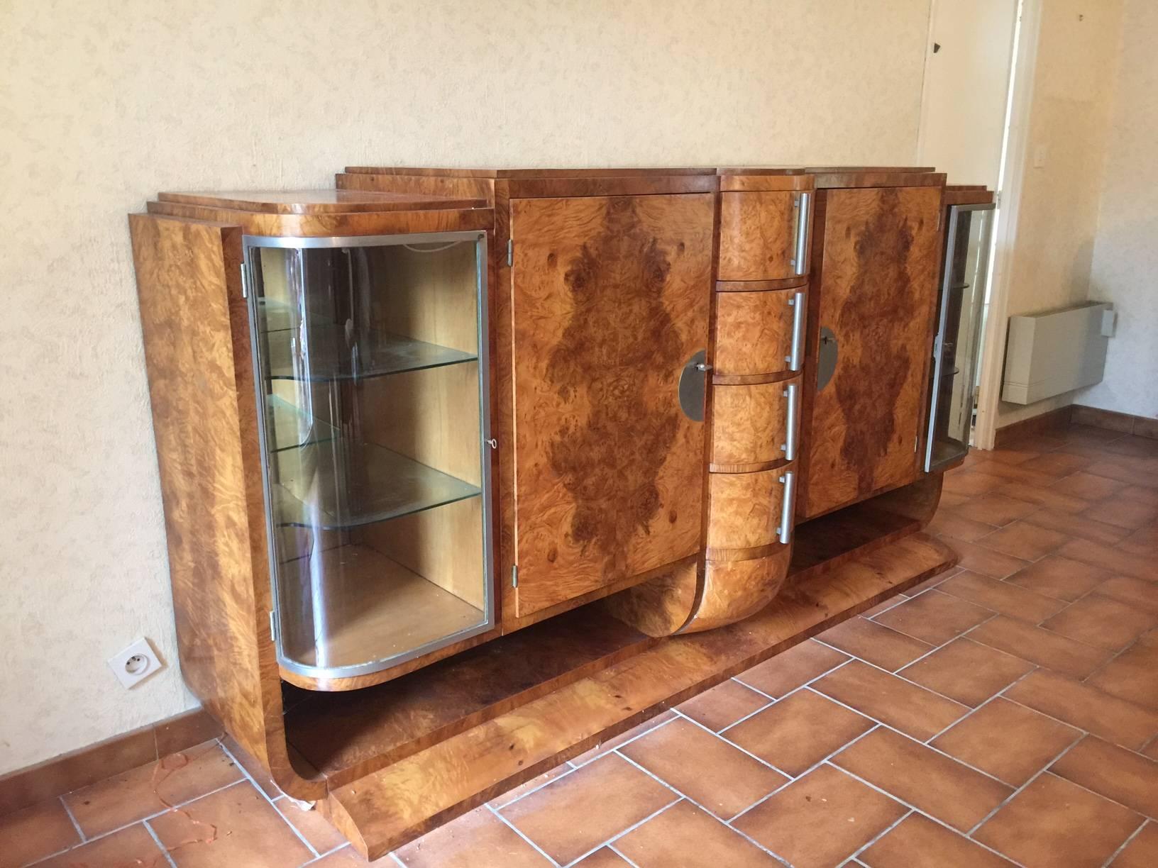 Large Art Deco burled elm buffet opening with two doors, four drawers and two glass doors.
Wood shelves behind the wood doors, mirror and glass shelves behind the glass doors.
Complete dining room set available.
 