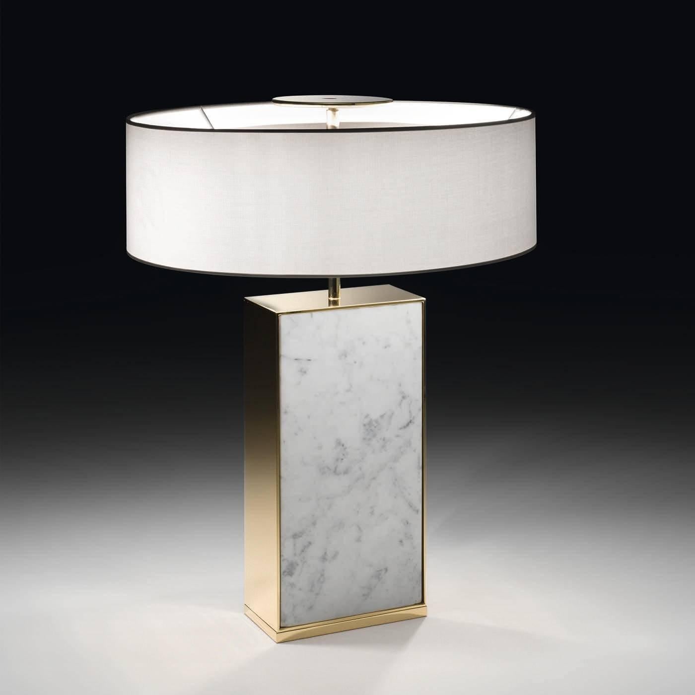 This striking lamp features a body in precious Carrara marble with gold-finished metal accents on the sides. The lampshade is in a firm fabric. A top metal element allows the lamp to project its light downward.