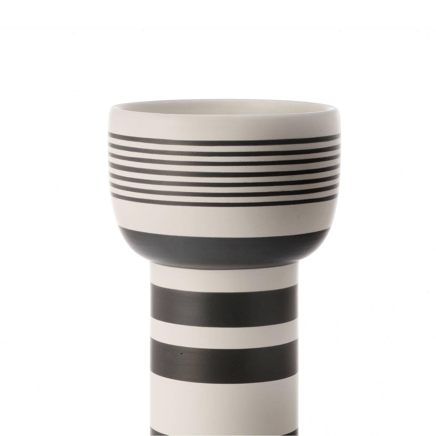 This elegant vase was designed by famous Italian architect Ettore Sottsass in 1962. It is in white clay and its geometric shape with a white finish is adorned with a series of parallel black lines of different thickness, for a striking final result.