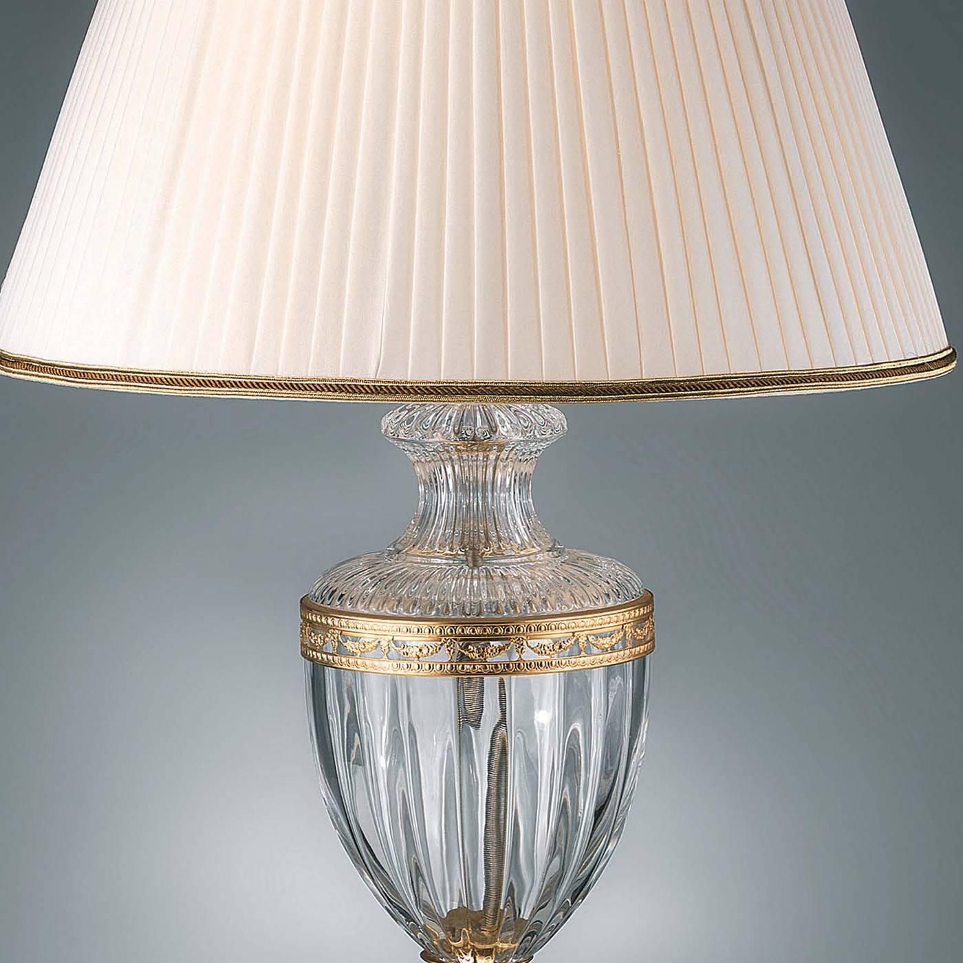 This lamp meant for the top of a dresser will add a touch of luxury to any home. The clear crystal body of the lamp is adorned with accents and a base in 24-karat gold plated brass. The elegant white lampshade has piping in its bottom and top in