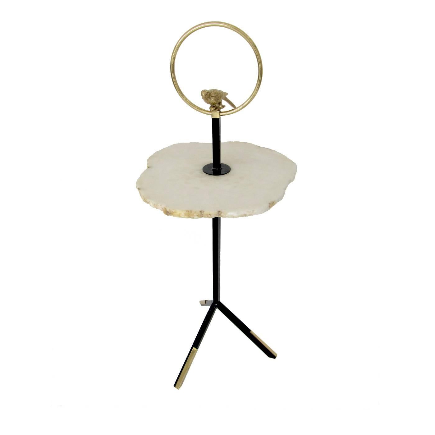 This table in polished iron has a top in natural alabaster with irregular edges. Melded brass accents at the base are reprised at the top with a decoration featuring an exquisite bird enclosed in a circle.