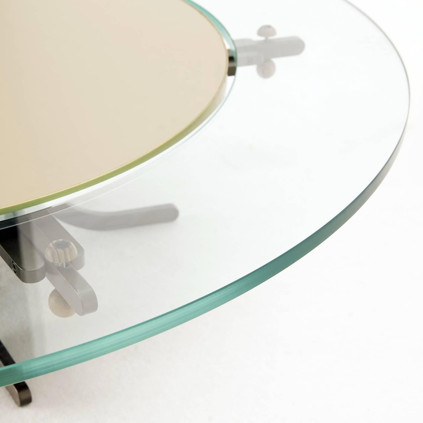 This unique coffee table features a top made of two disks: The glass edge is fixed, the central disk, hand-upholstered in leather, rotates to share and serve food. This striking top rests on an iron structure with visible brass details.