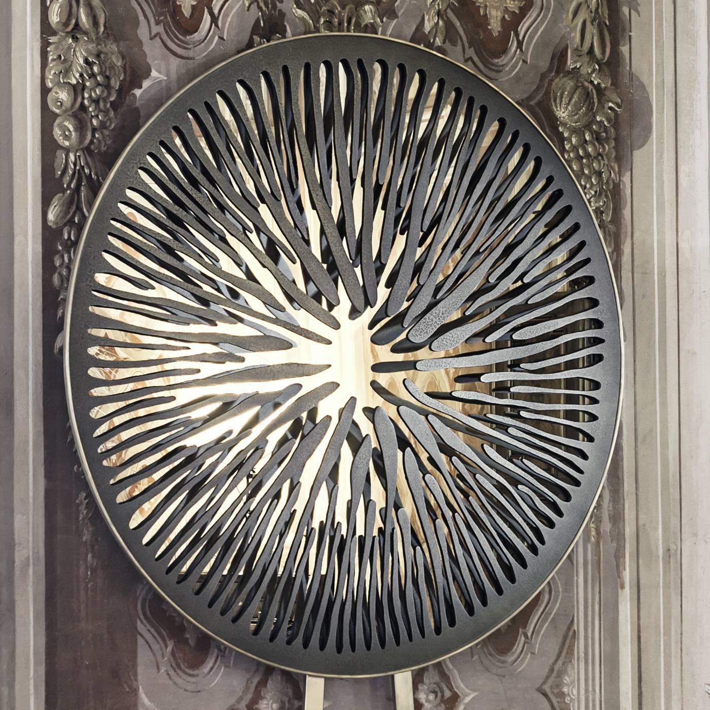 This ornate sculptural mirror's design was inspired by the pupil of an eye. The centre of the mirror is crafted in copper-plated aluminium with a dark green coating. The boarder is in wax coated brass with a bronze finish. This piece is the sole