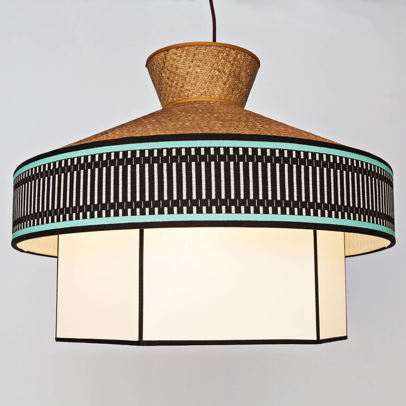 This chandelier has a structure crafted in rattan combined with the added component of a fabric featuring a geometric pattern on it. Its shape is similar to an old house with a straw roof. This piece was meant to give the feel of a lantern in a