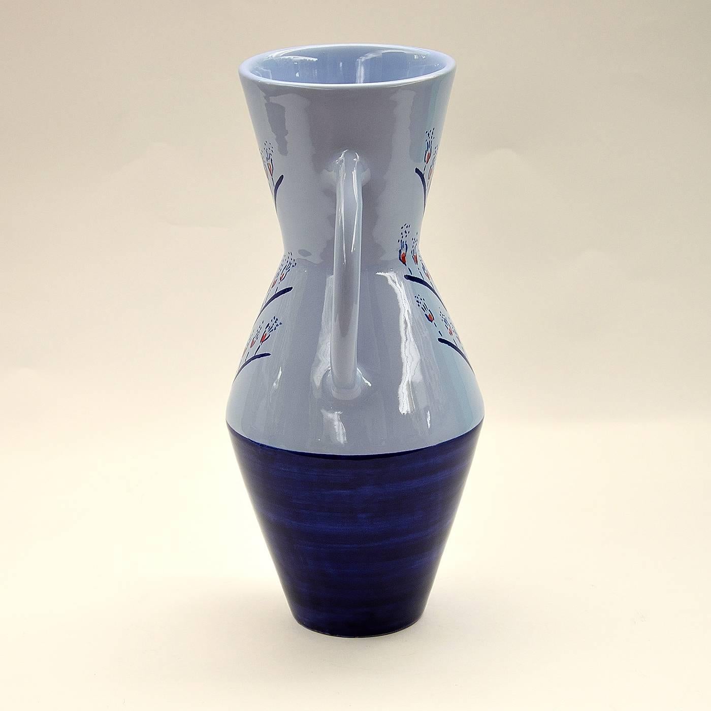 This stunning ceramic vase with handles was made on a lathe and enameled in earthenware. It was hand-painted in a beautiful deep blue at the foot and decorated with blue and red hand-painted designs over the glossy blue base. This piece is one in a