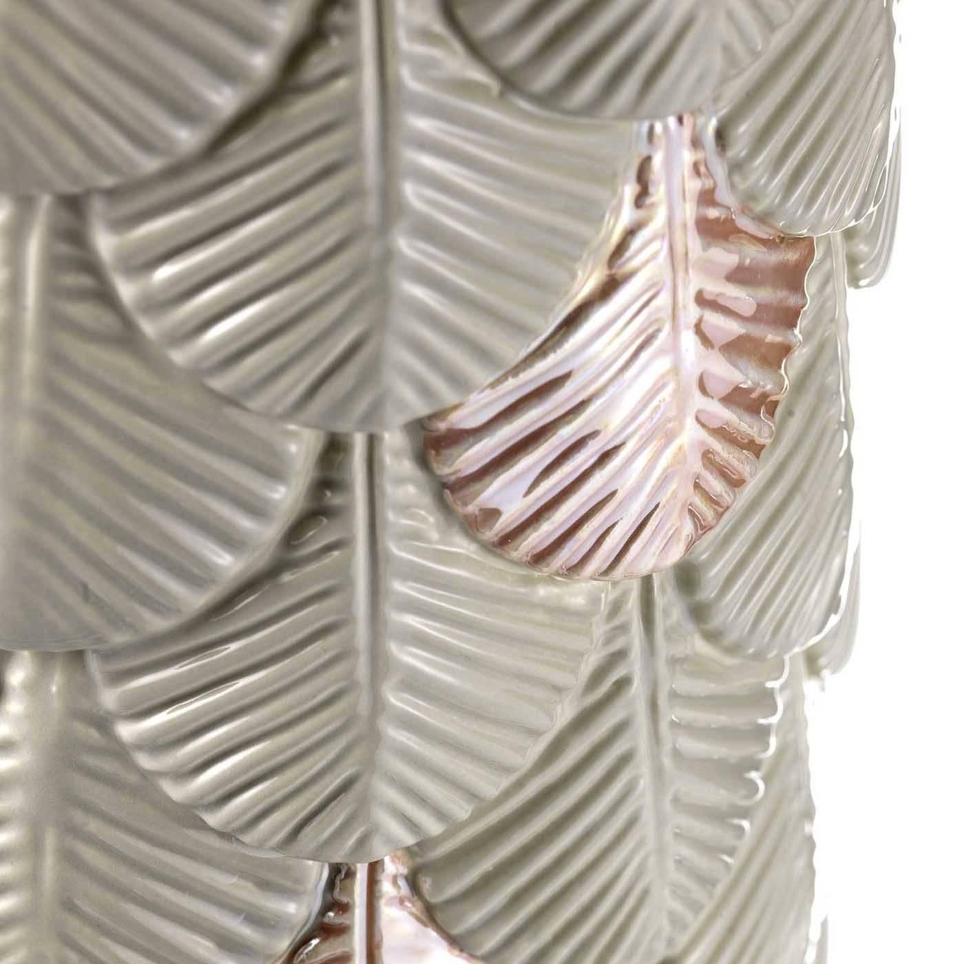This striking vase, designed for BottegaNove by Cristina Celestino, features a simple cylindrical shape adorned throughout by parallel rows of feathers with a hand-applied finish in grey with a green undertone. Here and there, the artisans who made