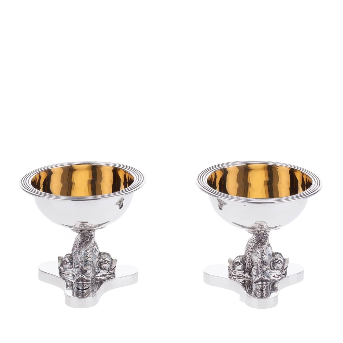 This is a pair of sterling silver salt cellars with a gold-plated interior by Florentine Silversmiths Pagliai. Modeled on a late 18th-century Venetian original, each cup is supported by three richly-detailed fish making up the stem.