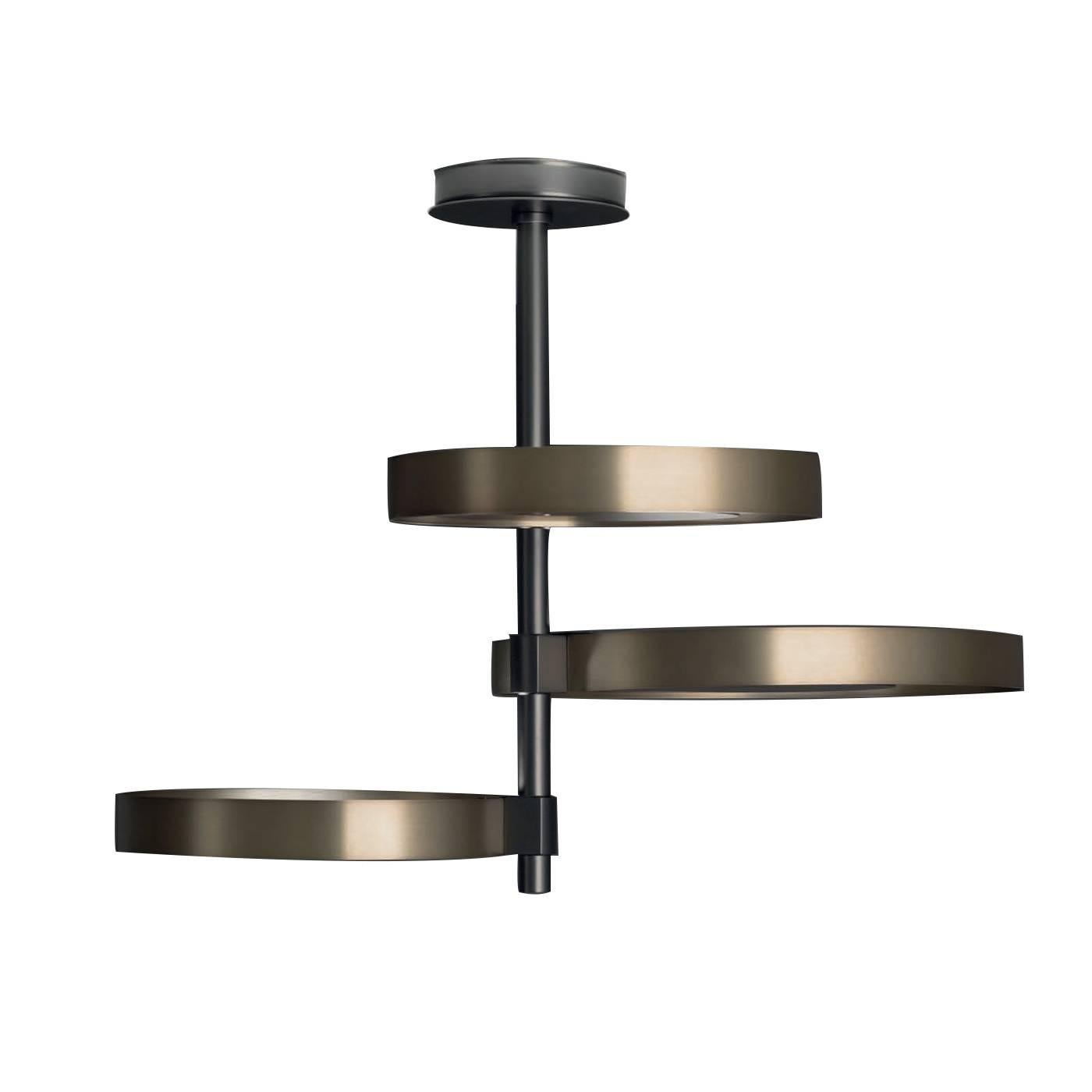 This ceiling lamp projects light upwards, thanks to its unique structure made of three satined natural brass rings enclosing three matte black nickel shades placed in different directions that shield the bulb and diffuse the light creating a