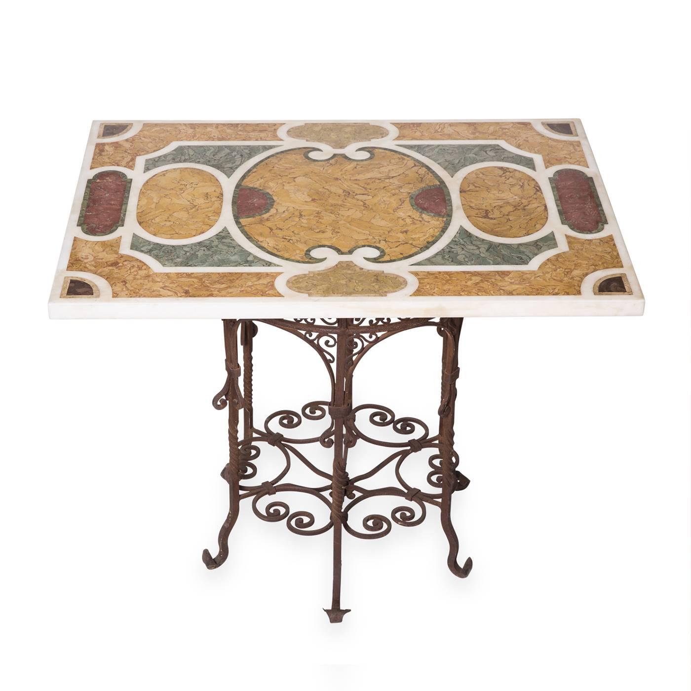 This handmade tabletop is an ode to the colors and shapes of Roman architecture and lifestyle. The white marble is inlaid with colorful marbles employing the traditional scagliola technique and rests on an antique, hand-forged wrought iron base.