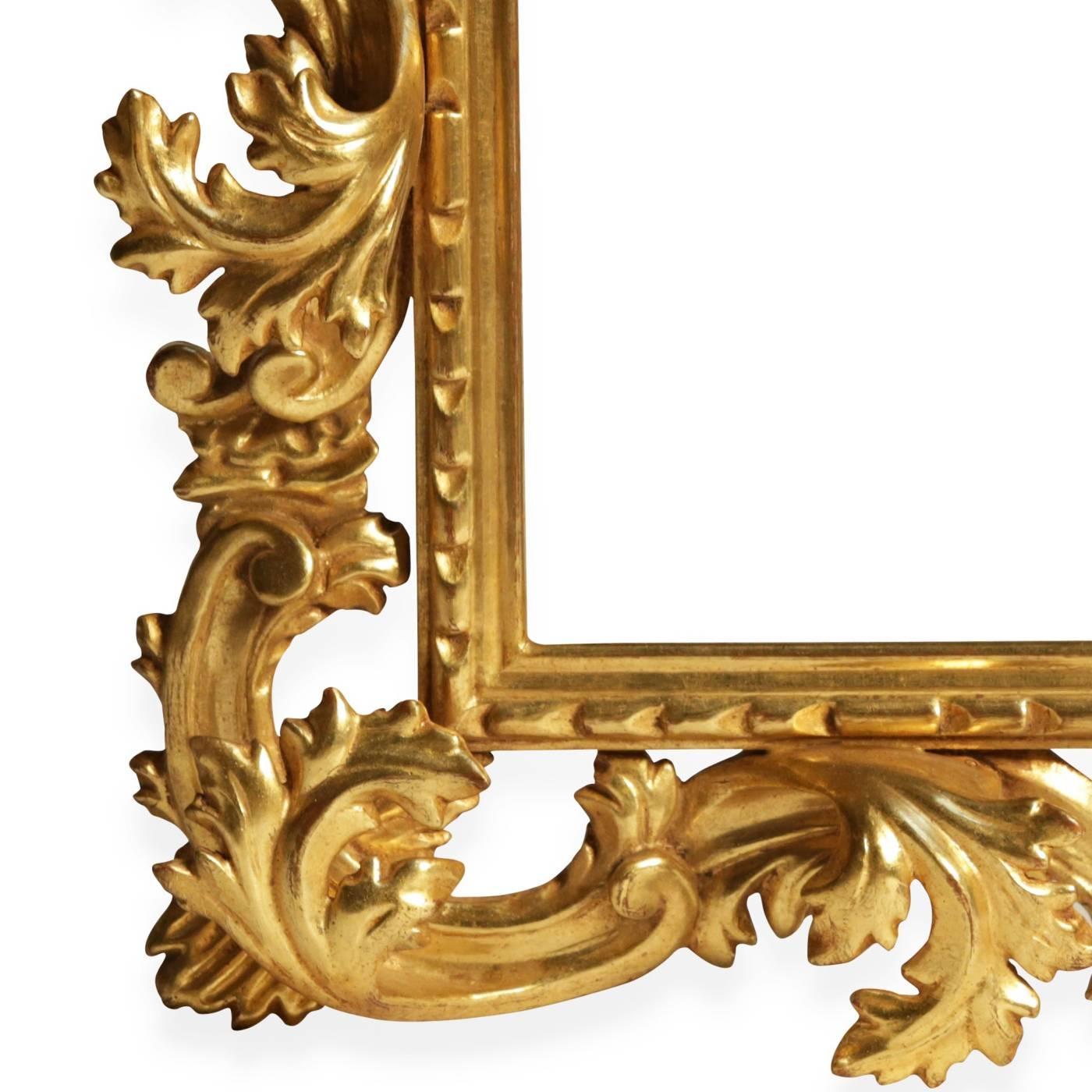 This piece is a handcrafted cartoccio framed mirror by Florentine wood carver Castorina. The frame is entirely engraved by hand and decorated in gold leaf with a burnished finish and an antique look. Also the mirror itself is treated to look