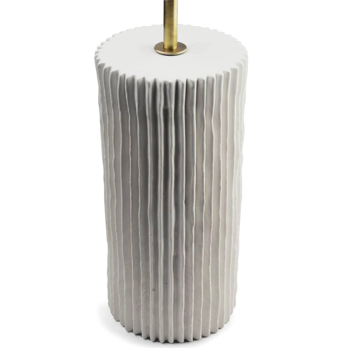 The base of this elegant lamp is a cylinder in white ceramic whose surface is decorated with ridges throughout. The body is in brass with a cylindrical diffusor that features a decoration of vertical ridges as well.