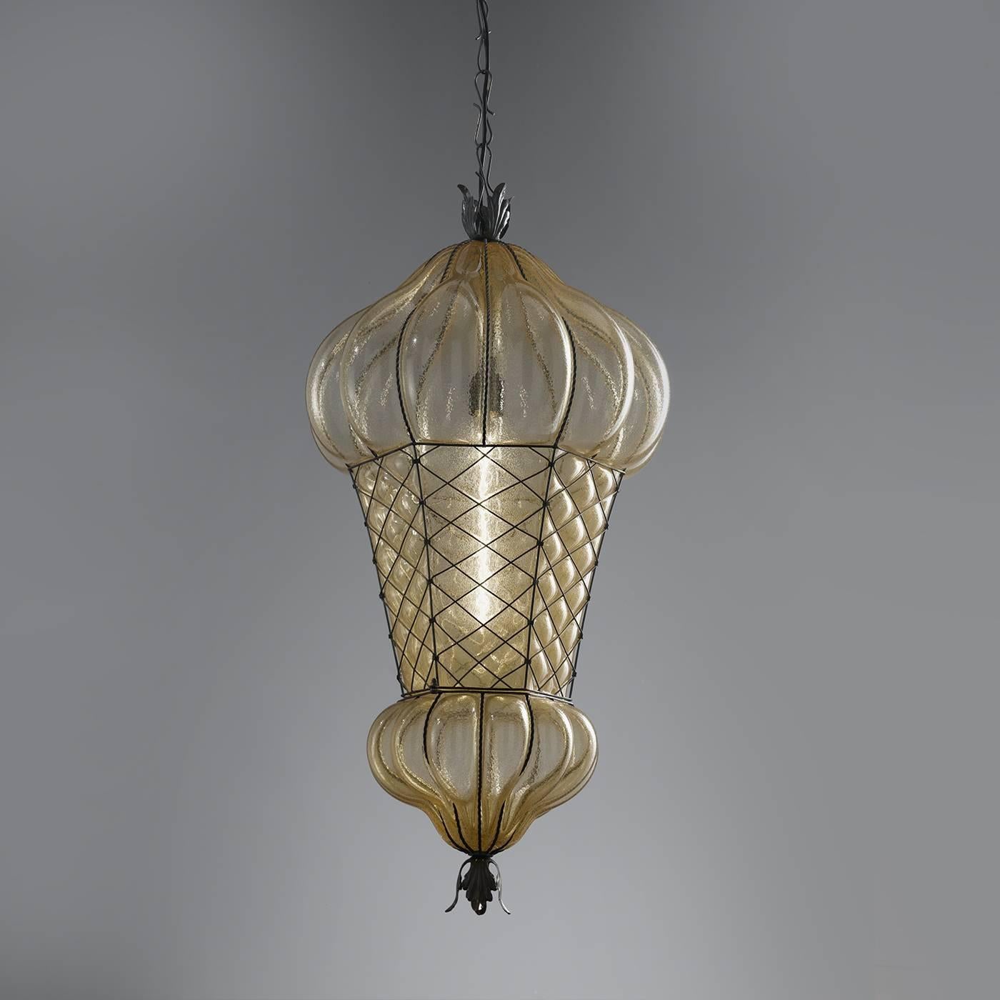 This magnificent lamp will add a touch of opulence to a living room, thanks to the amber color of its Murano glass shade and the sinuous shapes of the bronzed steel structure. The glass is mouth-blown into the structure that encapsulates it,