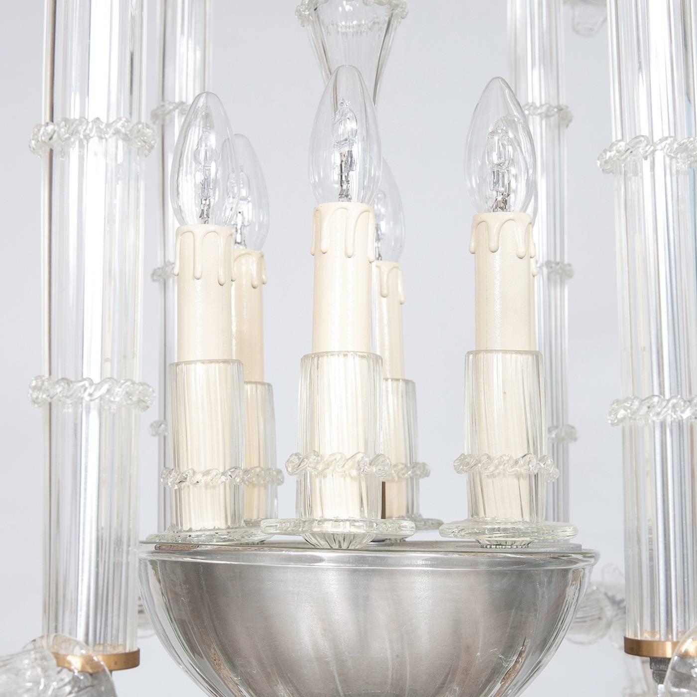 The Cesendello chandelier was entirely crafted in transparent Murano glass and is composed of a central element with six uprights surrounding a group of six outward-facing lights, illuminating all in all directions. On the top and bottom of the