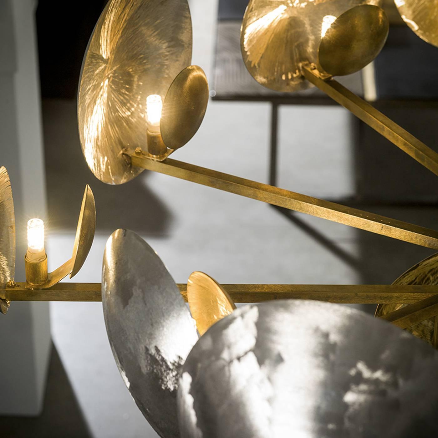 This striking chandelier will make a grand statement when placed in any room in the home. A series of arms extend from a central round element, both finished in natural brass and on the end of each arm is an illuminating element and a large disk