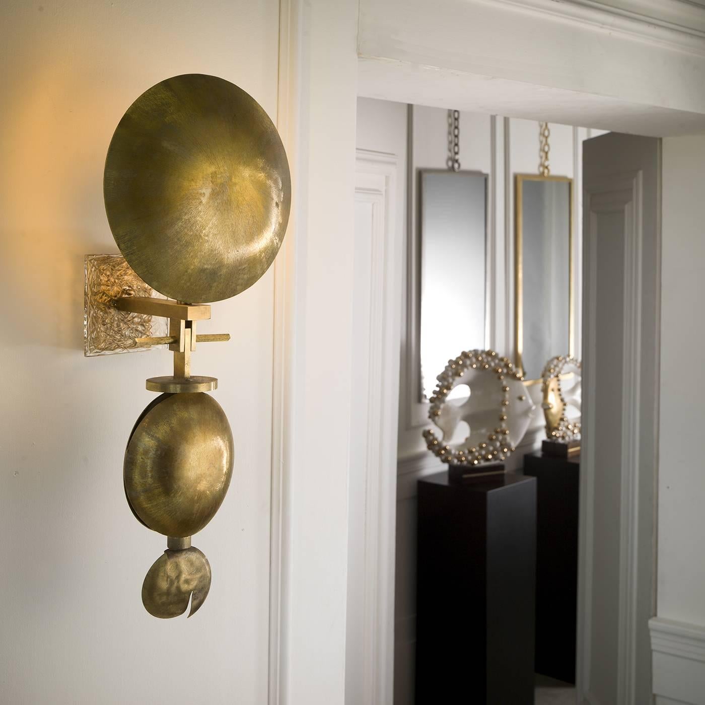 This sconce will best complement a contemporary environment with its impressive structure composed of three natural brass discs arranged in a linear configuration from largest to smallest. The fabric-like texture given to the brass discs was