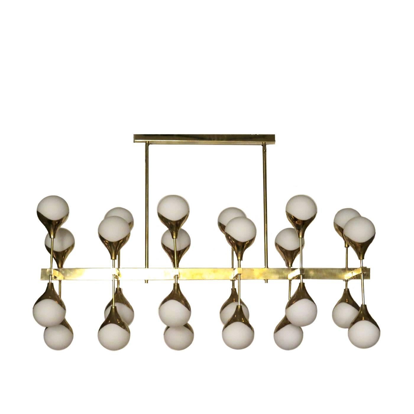This imposing chandelier is composed of twenty-four lights enclosed in white glass spheres. The structure is in elegant brushed brass and consists of a long rod supported by a shorter stick attached to the ceiling. The lights are paired in two and