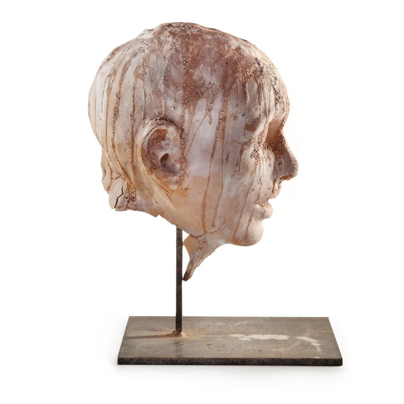 Unusual terracotta sculpture on an iron base, executed irregularly so as to convey the simultaneous concepts of construction and deterioration, two essential aspects of life, with closed eyes and a mostly rough surface on the scalp and complexion.