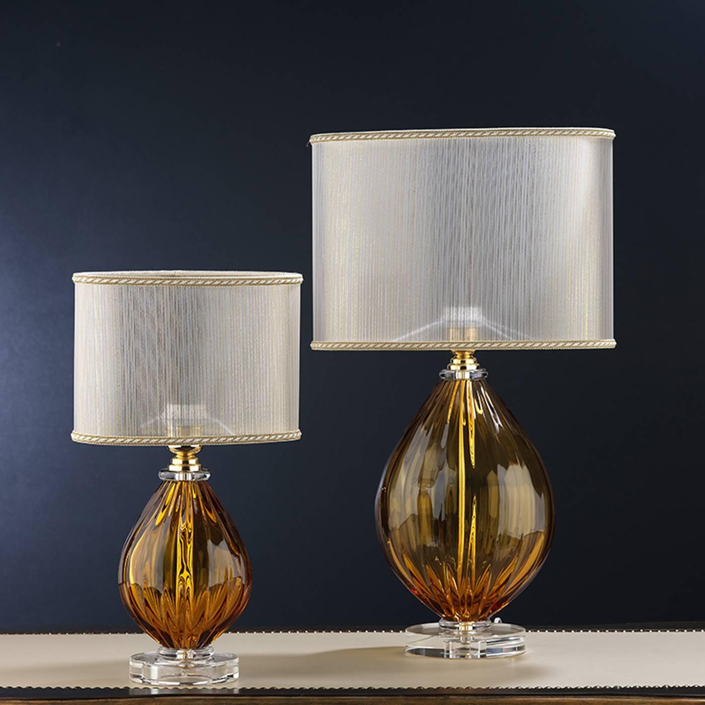 This elegant lamp was designed to sit on a bedside table. Its body is crafted in mouth-blown crystal in a rich amber coloration, with a clear base. The transparent lampshade harmoniously complements the body.