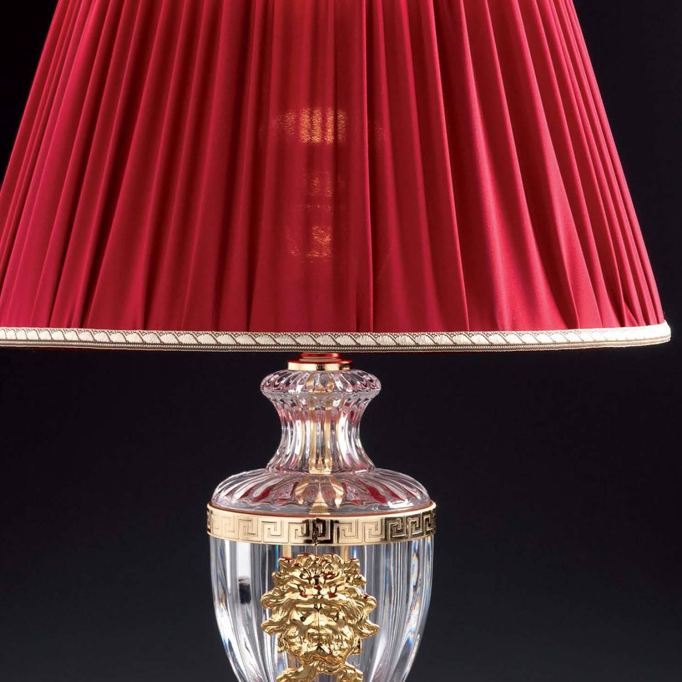 Le corps de cette lampe élégante est fabriqué en cristal clair et est orné d'éléments en laiton plaqué or 24 carats. La base est également en laiton plaqué or 24 carats. La lampe est surmontée d'un riche abat-jour rouge pour un effet luxueux.