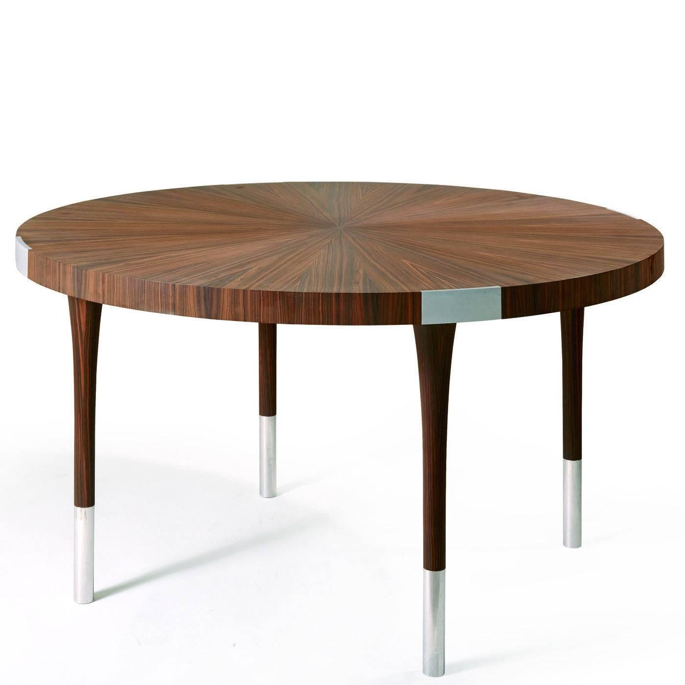 This elegant round table in ebony Macassar wood with its distinctive dark brown strikes, features inserts in aluminum with a satin finish. The top is veneered with a traditional 'sun ray' inlay technique, where the veining of the outer layers are